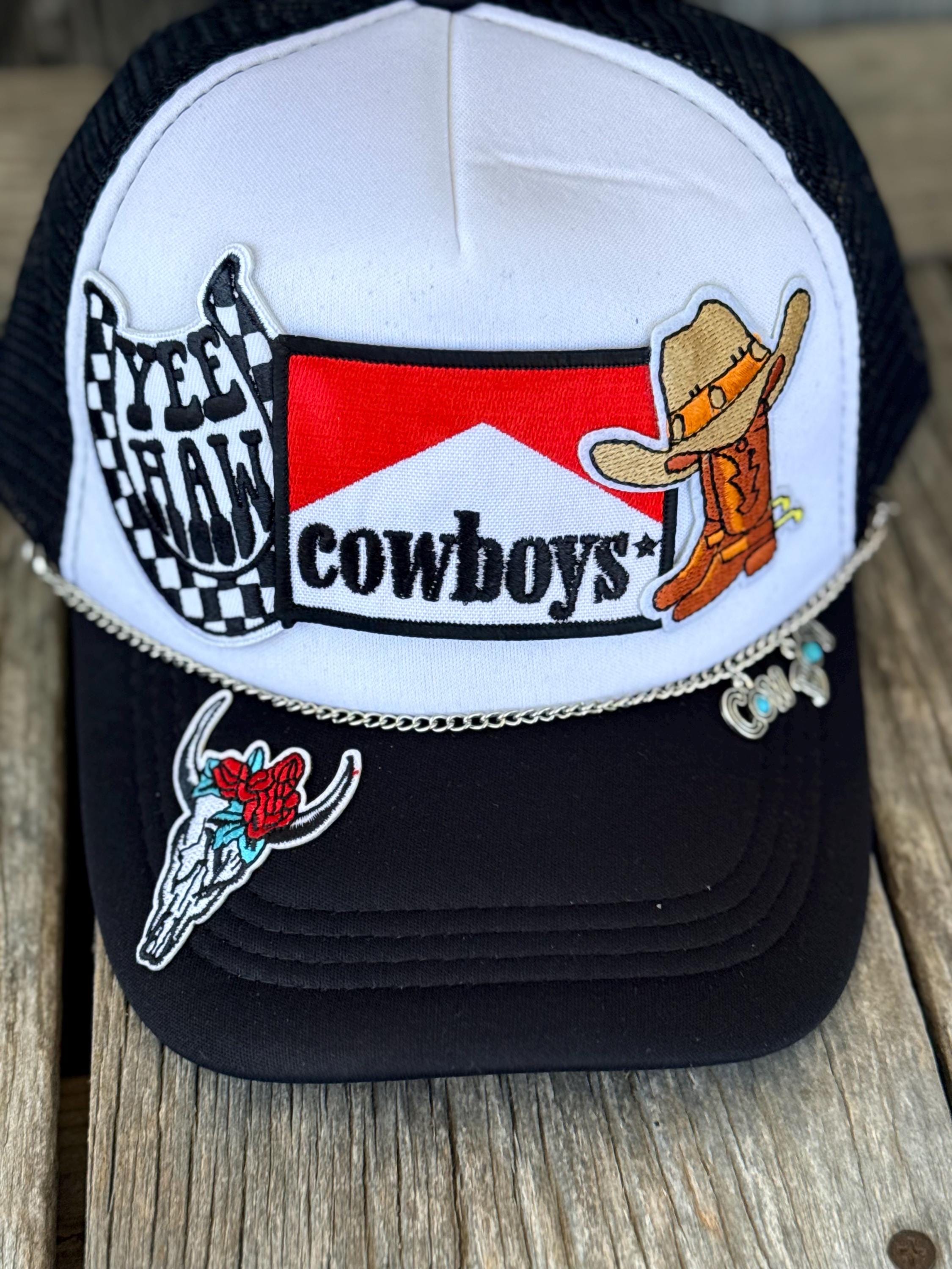 A western-themed trucker hat with a white front panel, black mesh back, and black brim, decorated with embroidered patches including a cowboy boot, a skull with a rose, and a checkered flag design.