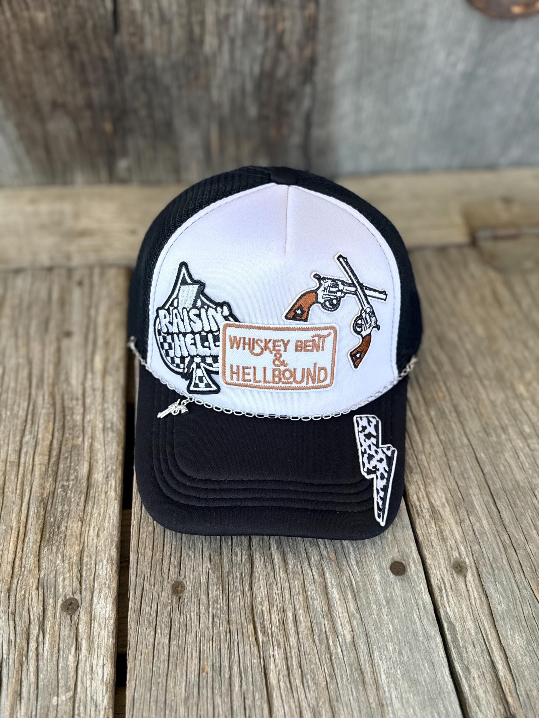 A black and white trucker hat with embroidered graphics on a rustic wooden surface. The front panel is white with black mesh, featuring a brown and white 'Whiskey patch and cowboy/horse embroidery.