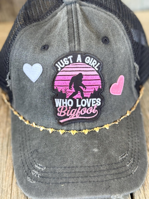 "Just A Girl Who Loves Bigfoot" Black Distressed Ponytail Trucker Hat | Bigfoot Patch & Gold Heart Hat Chain