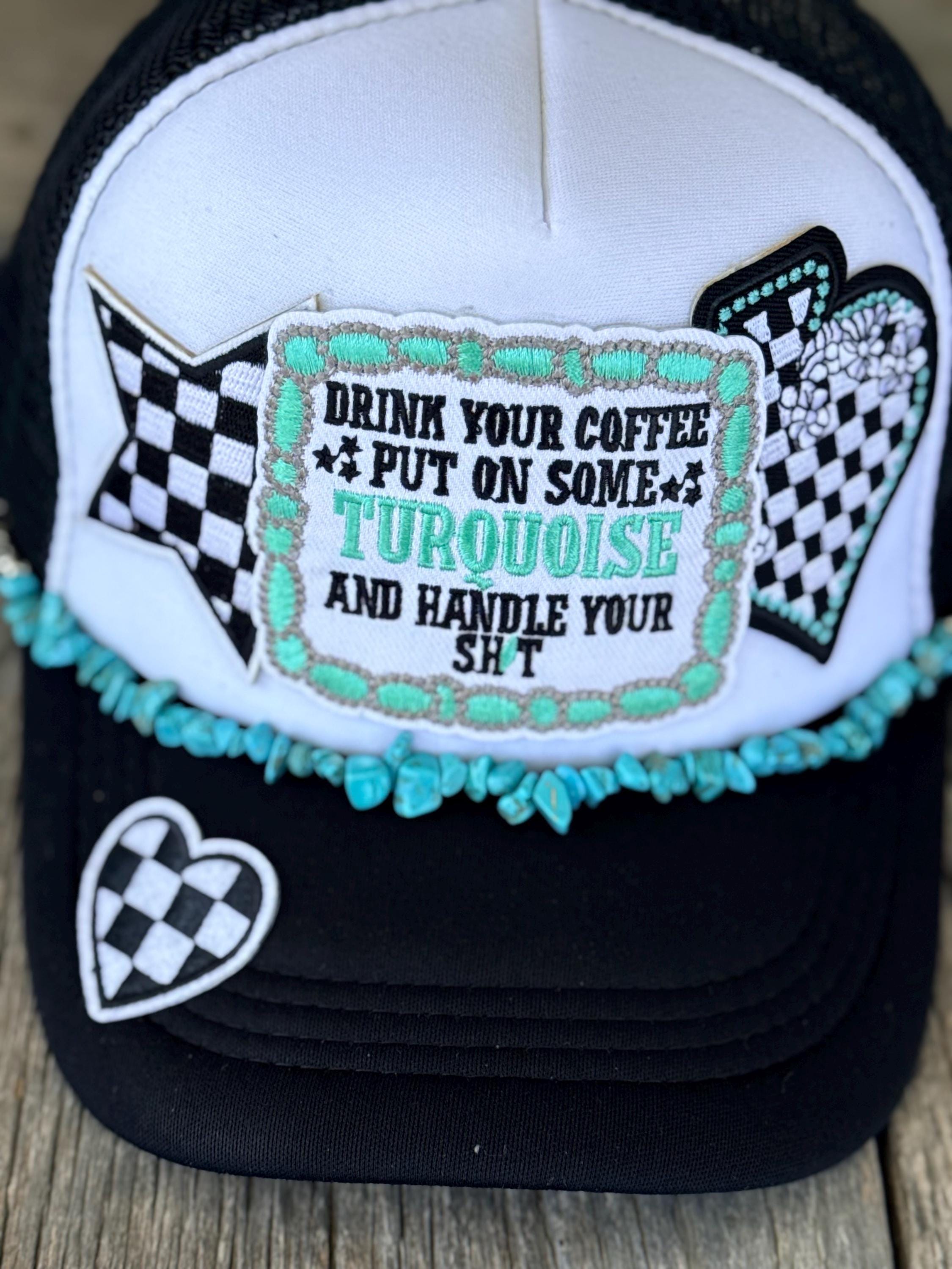 A trucker hat with a white front panel and black brim, decorated with a turquoise and black checkered patch that reads 'DRINK YOUR COFFEE PUT ON SOME TURQUOISE AND HANDLE YOUR SH*T'. The brim also features a small black-and-white checkered heart patch and a turquoise beaded trim.