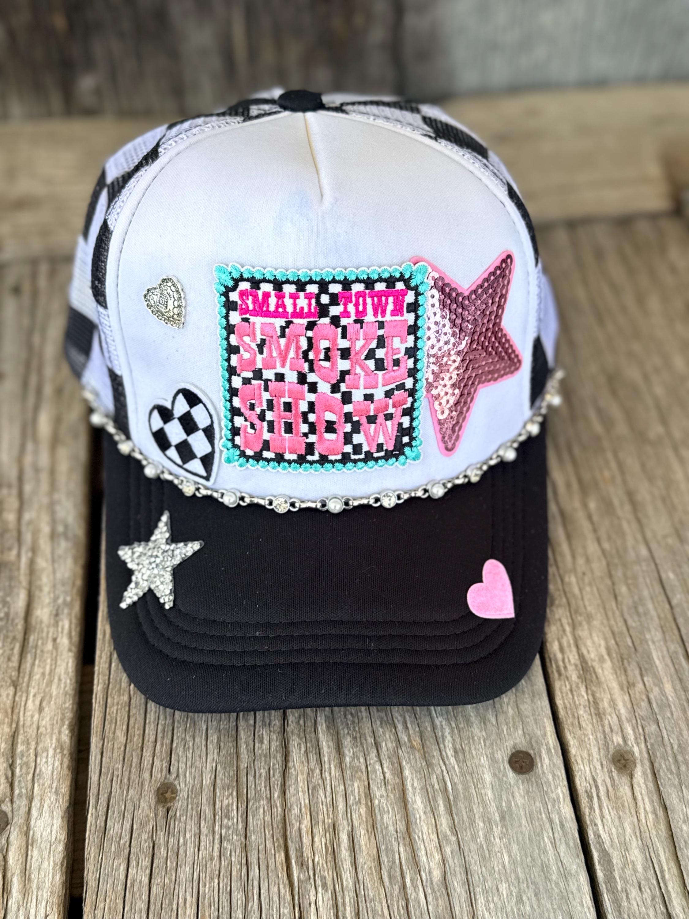 A customized trucker hat with a white front panel, black brim, and black-and-white checkered mesh back. The front is decorated with a central pink and black rhinestone patch, a pink sequined star, a black-and-white checkered heart, a silver heart, and a pink heart on the brim.