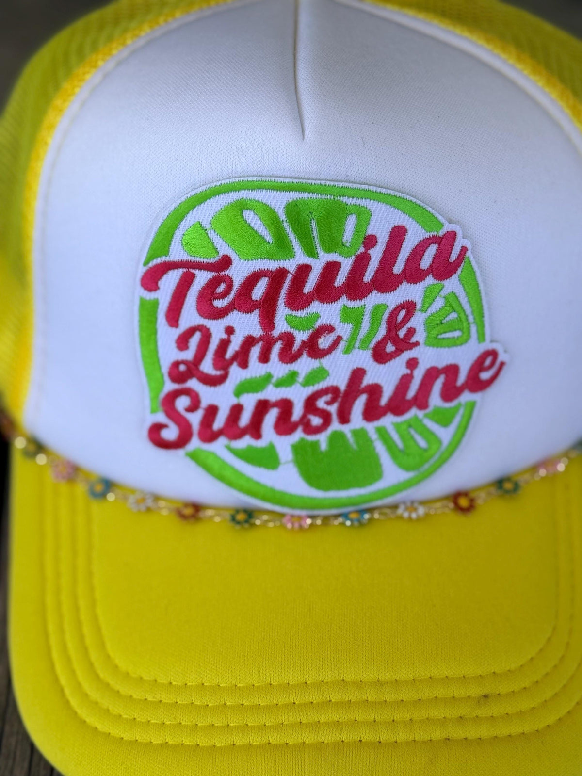 A close-up of a yellow and white trucker hat featuring a custom embroidered patch on the front. The patch displays a green lime slice design with the text 'Tequila Lime & Sunshine' in red script.