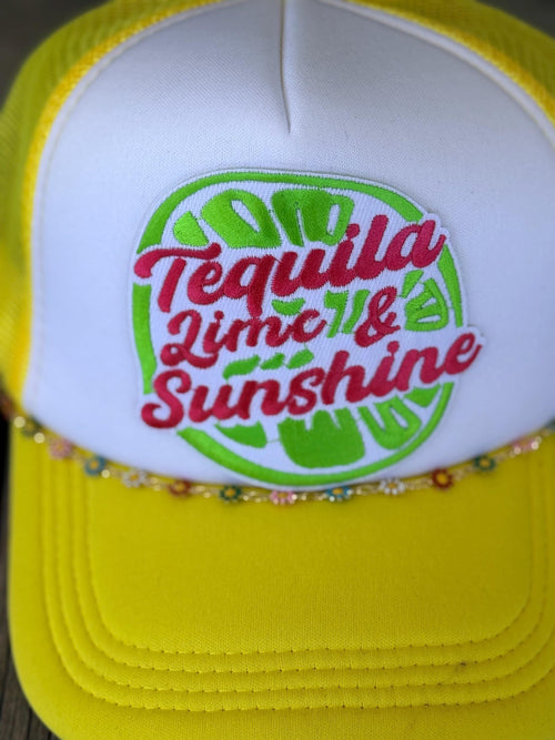 A close-up of a yellow and white trucker hat featuring a custom embroidered patch on the front. The patch displays a green lime slice design with the text 'Tequila Lime & Sunshine' in red script.