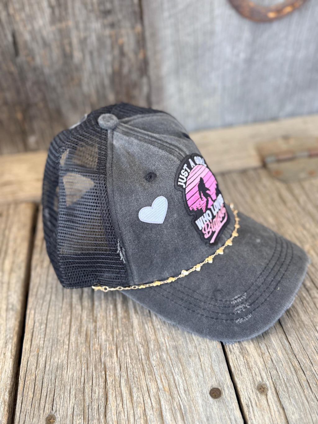 "Just A Girl Who Loves Bigfoot" Black Distressed Ponytail Trucker Hat | Bigfoot Patch & Gold Heart Hat Chain