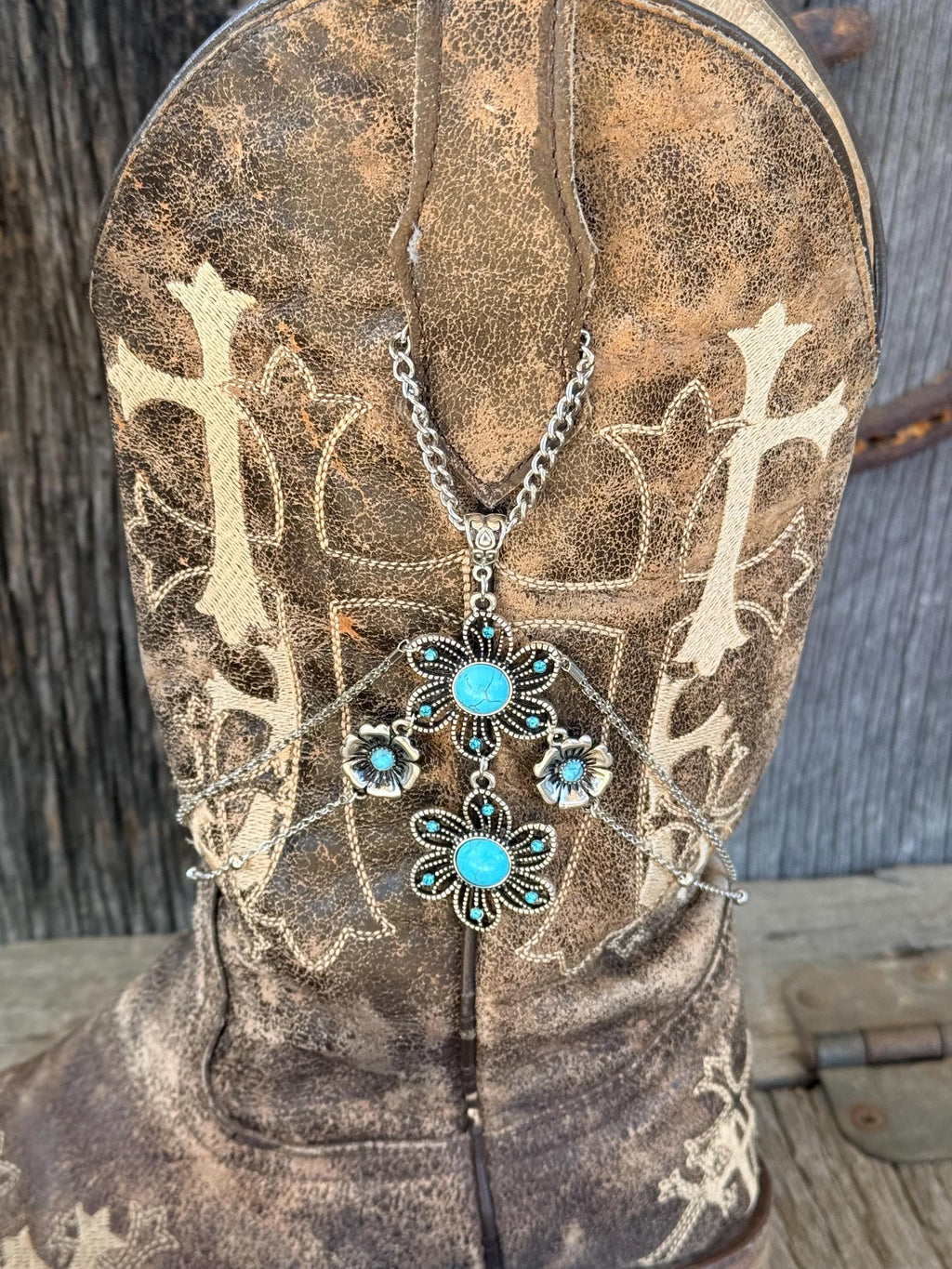 Close-up of distressed brown cross embroidered cowboy boot shaft with silver chain boot bracelet and large turquoise stone flower charm cluster pendant, Western boho boot jewelry