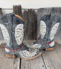 Front view of pair of dark gray distressed angel wing embroidered cowboy boots on weathered wood planks wearing red AB oval crystal and dark teal iridescent bead boot bracelets with large ornate silver filigree cross pendant, Western boot bling set of 2