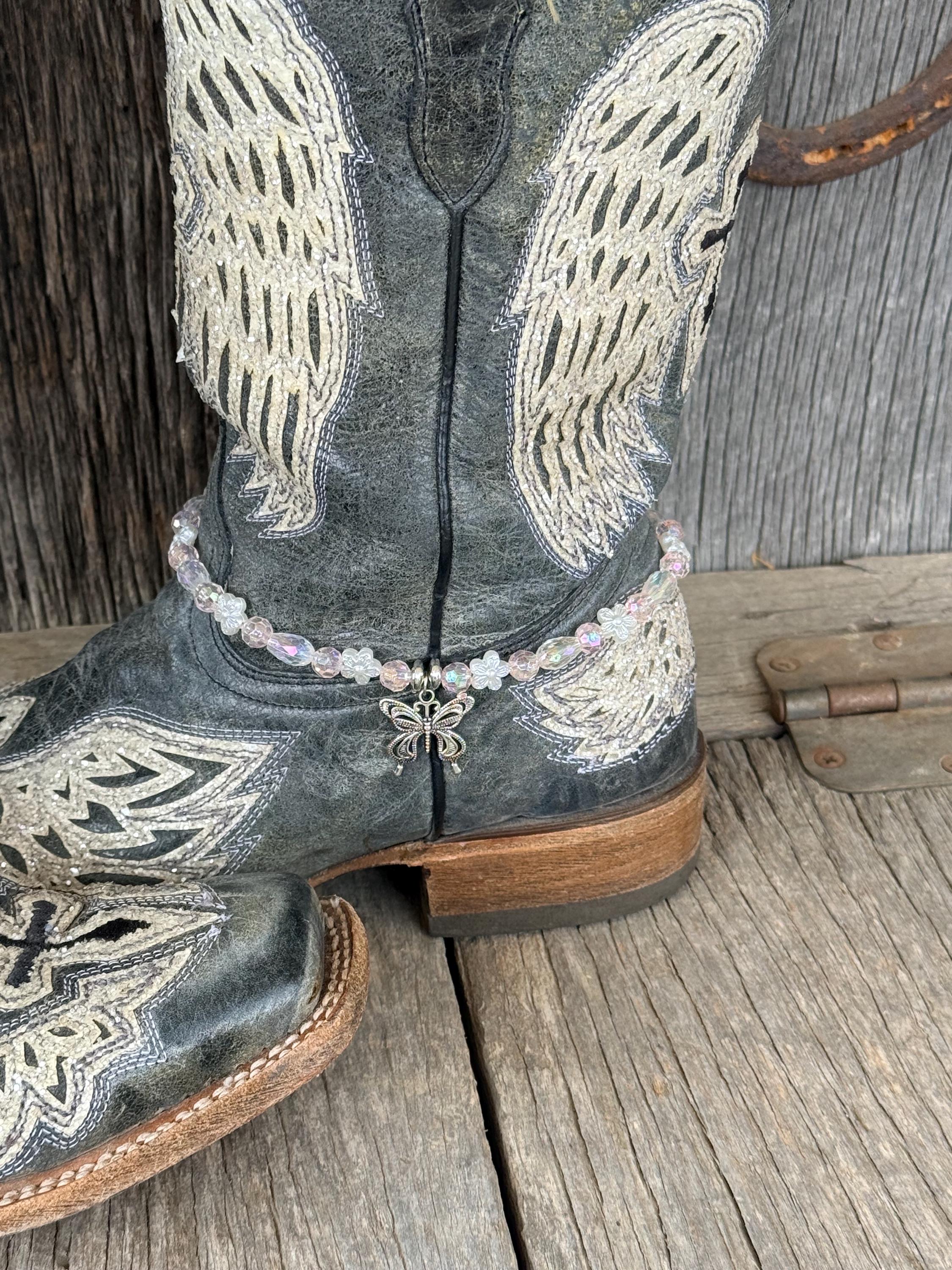 Front view of dark gray distressed angel wing embroidered cowboy boot with clear iridescent crystal and white flower bead boot bracelet and silver filigree butterfly charm pendant, Western boho boot jewelry