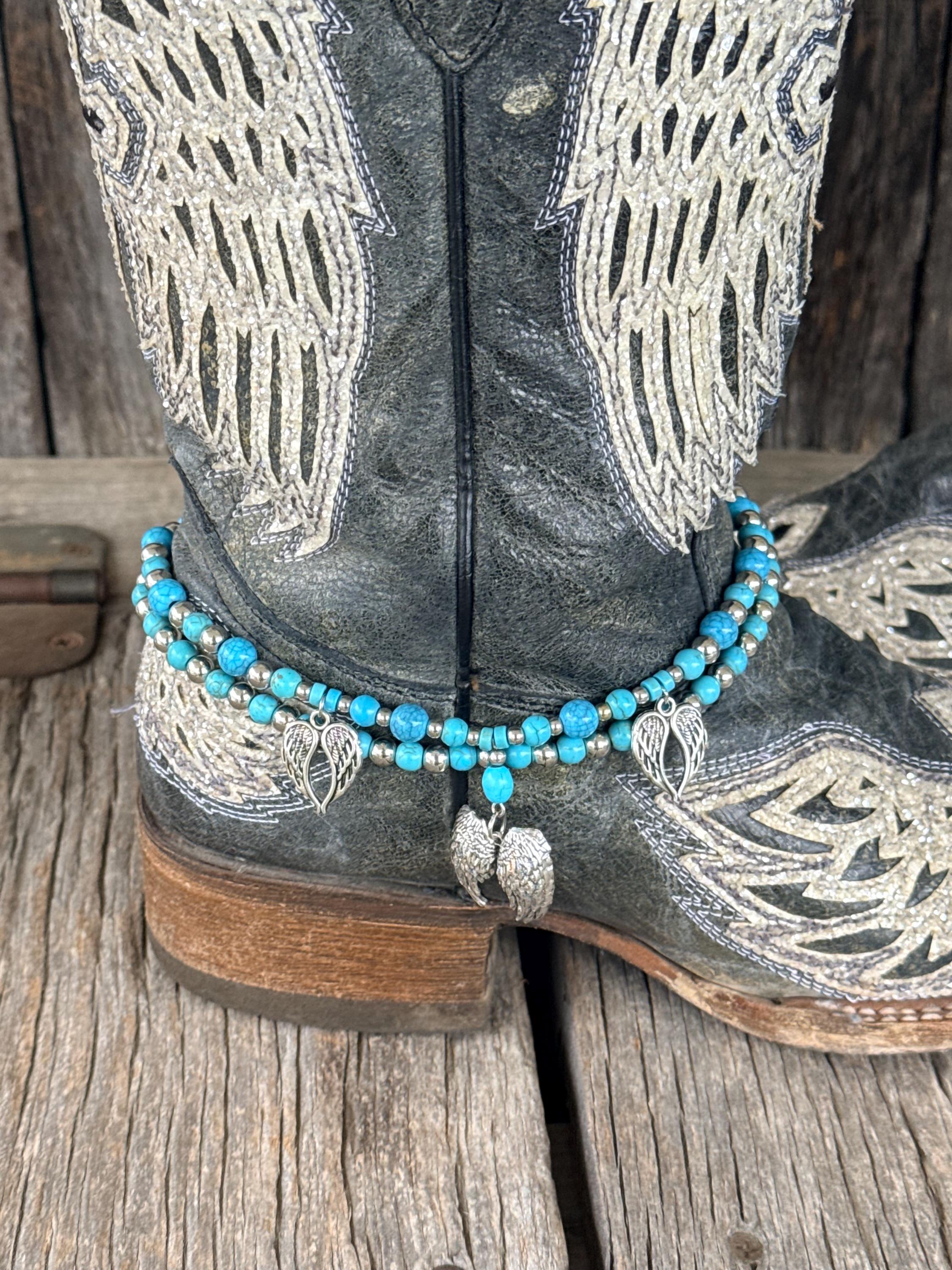 A close-up of a western boot with turquoise blue and silver beaded ankle bracelets resting around the ankle, set against a rustic wooden background.