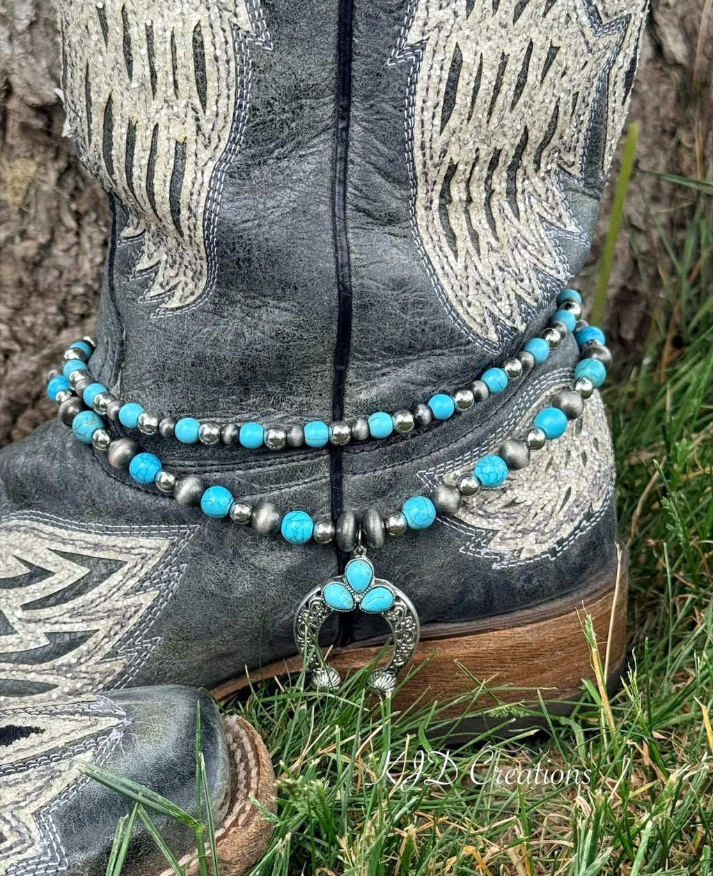 Front view of black distressed angel wing cowboy boot with two-strand turquoise and oxidized silver bead boot bracelet and silver filigree squash blossom naja pendant, Western boho boot accessory
