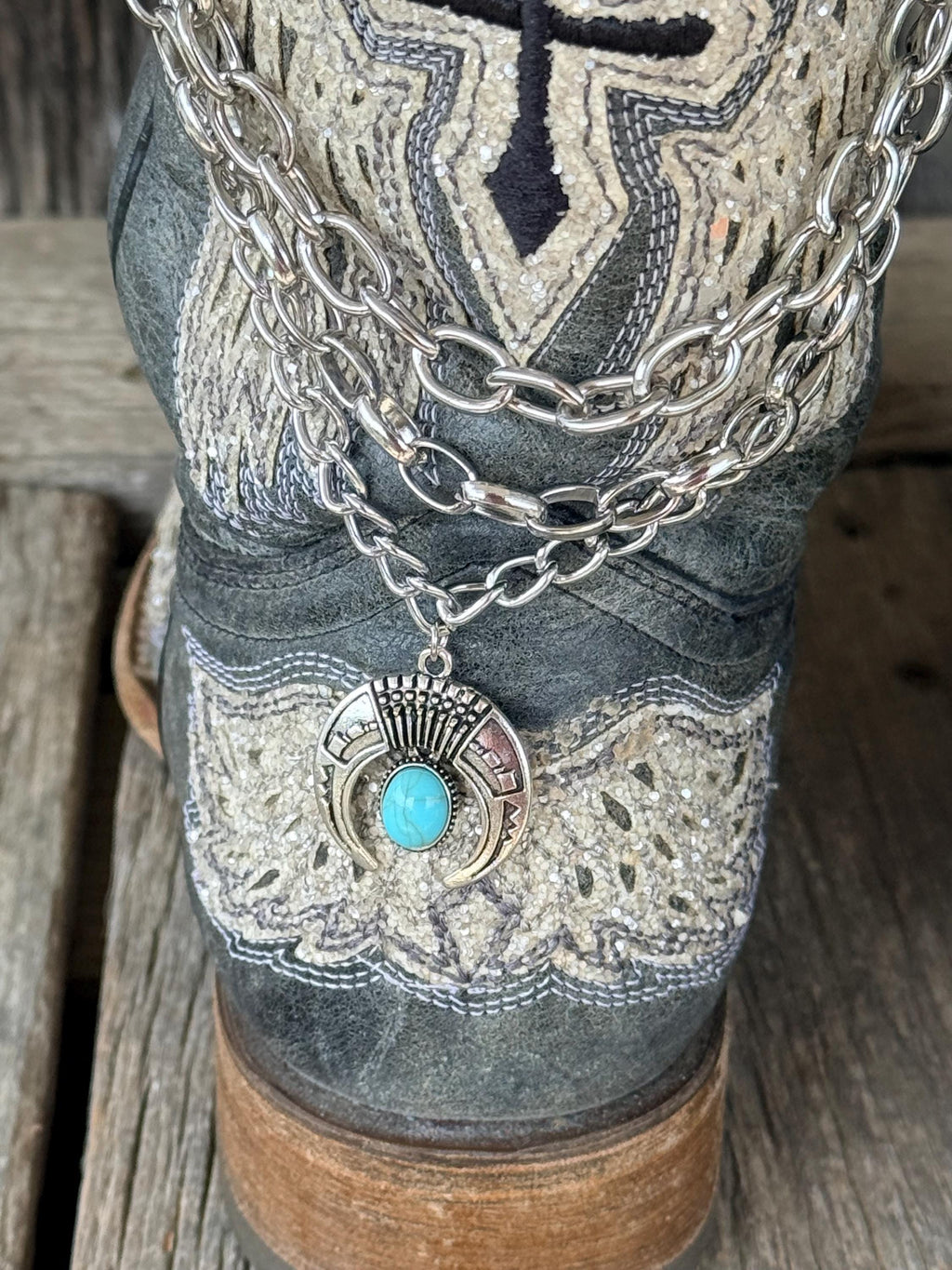 Close-up of layered silver chain boot bracelet on distressed gray cross embroidered cowboy boot with turquoise squash blossom charm pendant