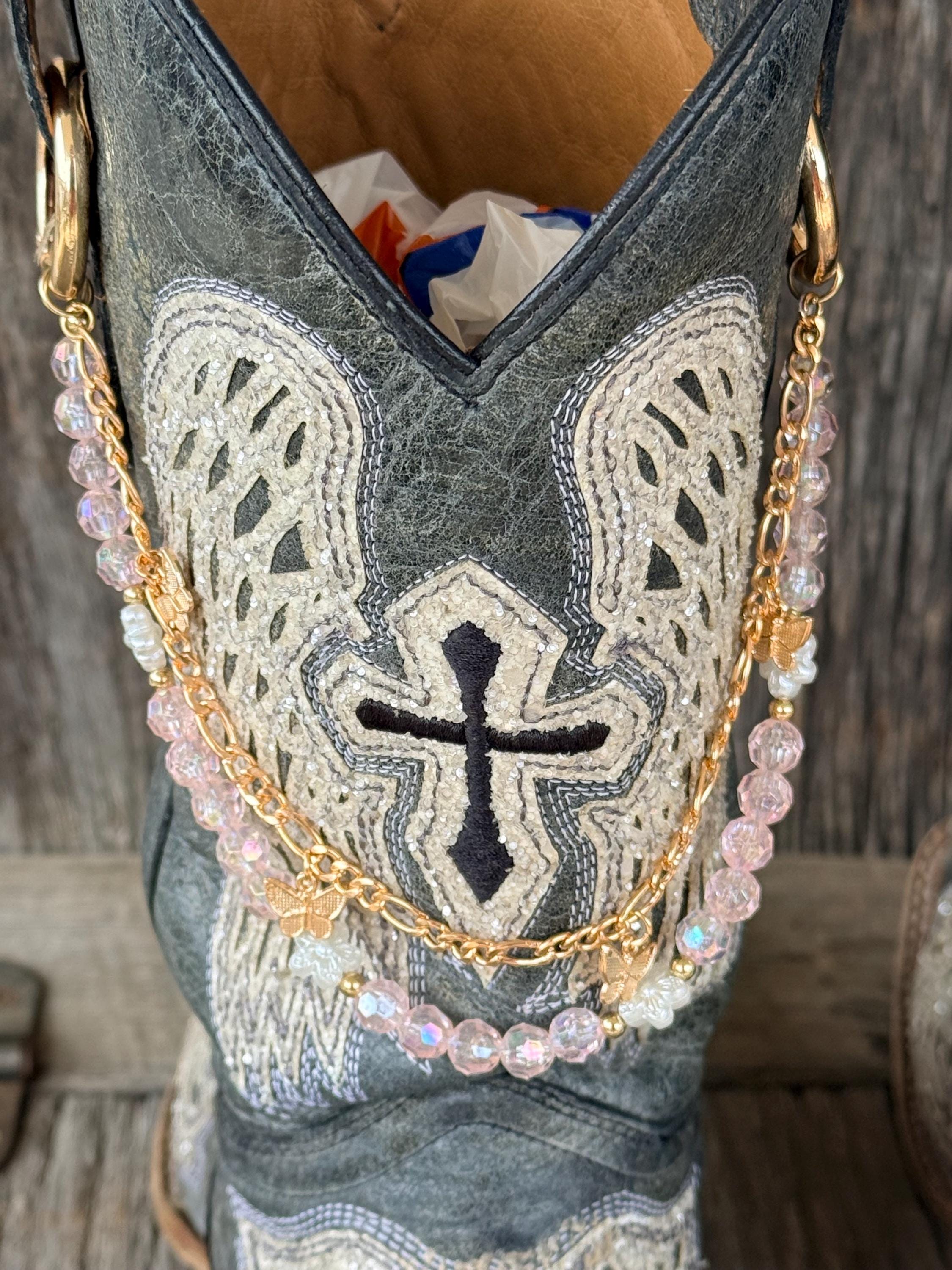 Close-up of grey cross embroidered cowboy boot wearing gold link chain and iridescent pink crystal bead boot bracelet with gold butterfly charm, Western boho boot jewelry