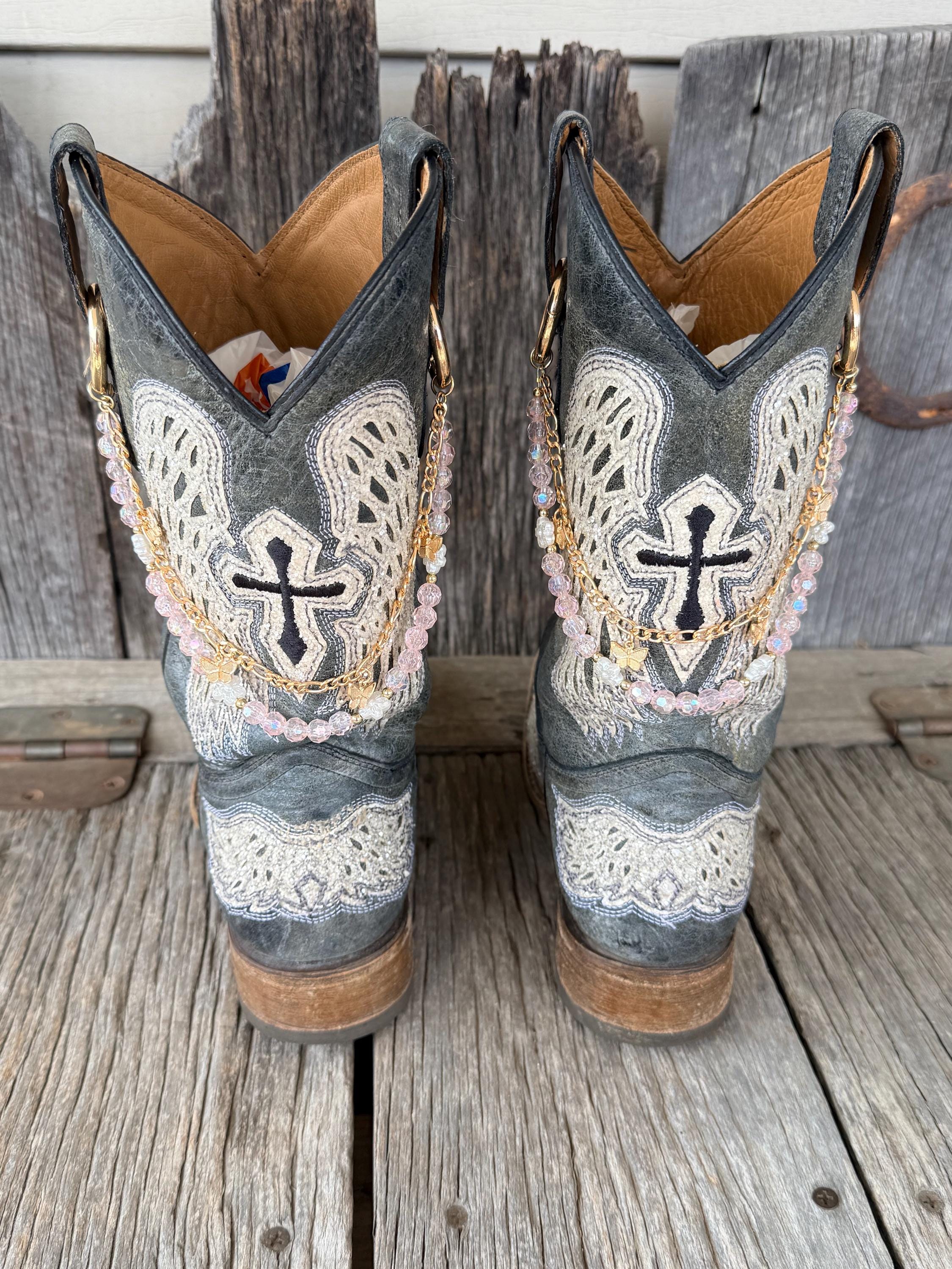 Back view of pair of grey cross embroidered cowboy boots wearing gold link chain and iridescent pink crystal bead boot bracelets with gold butterfly charm, set of 2