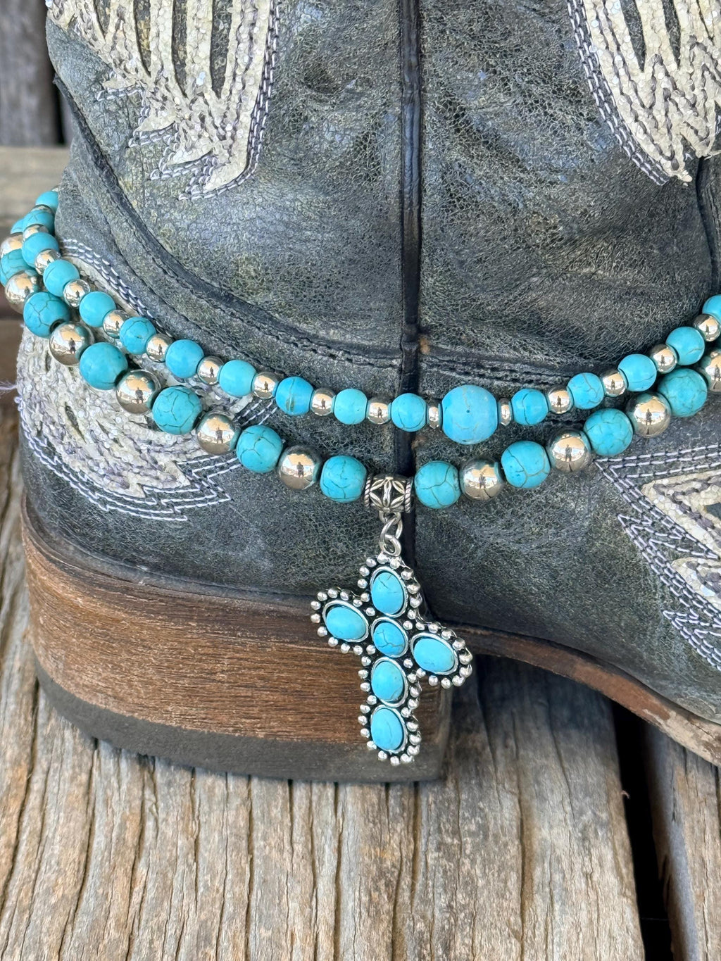 Back heel view of double-strand turquoise and silver beaded boot bracelet with turquoise cross charm on black embroidered Western cowboy boot