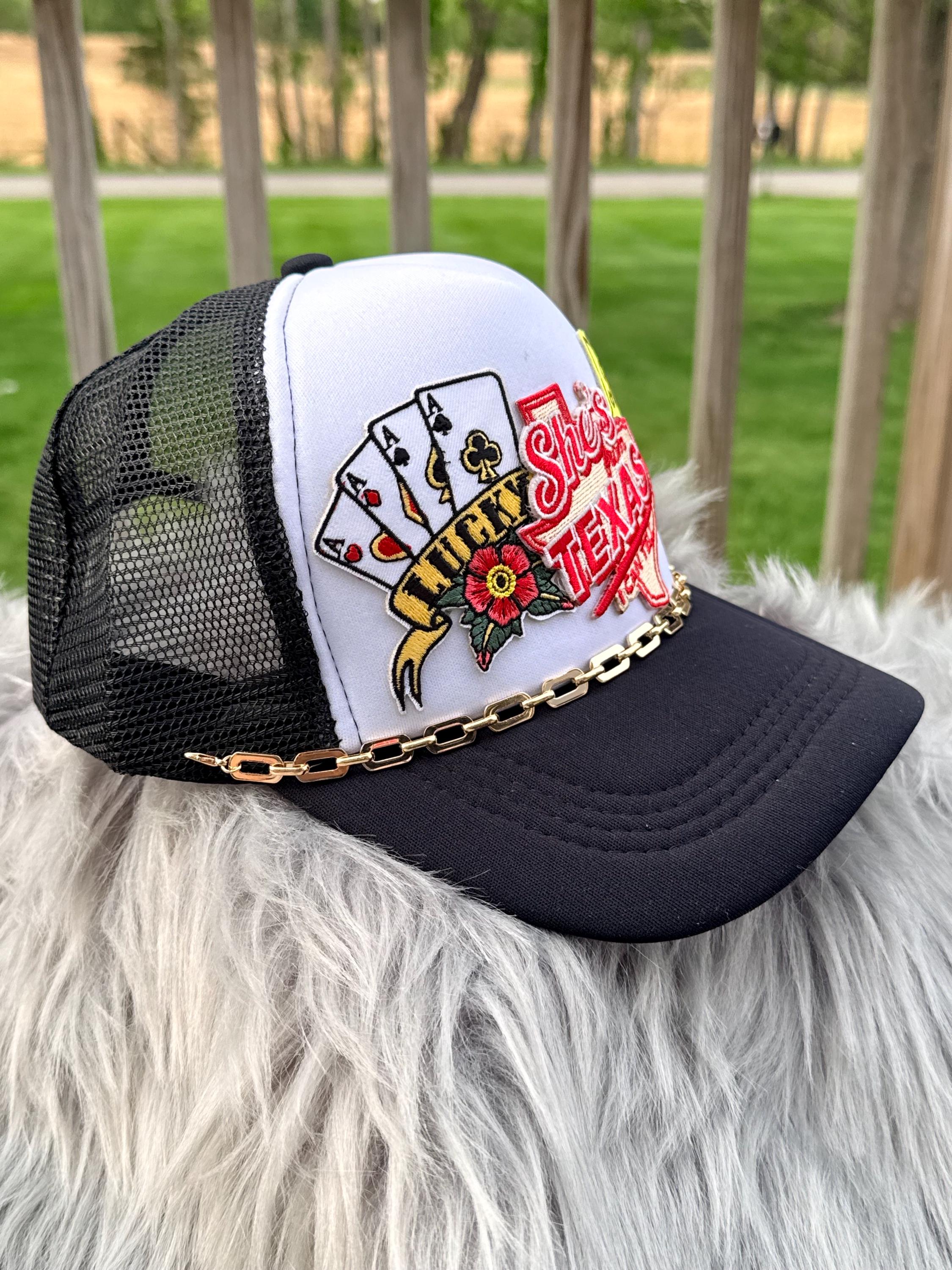 A black and white trucker hat with a gold chain detail, featuring a custom playing card graphic on the front, 