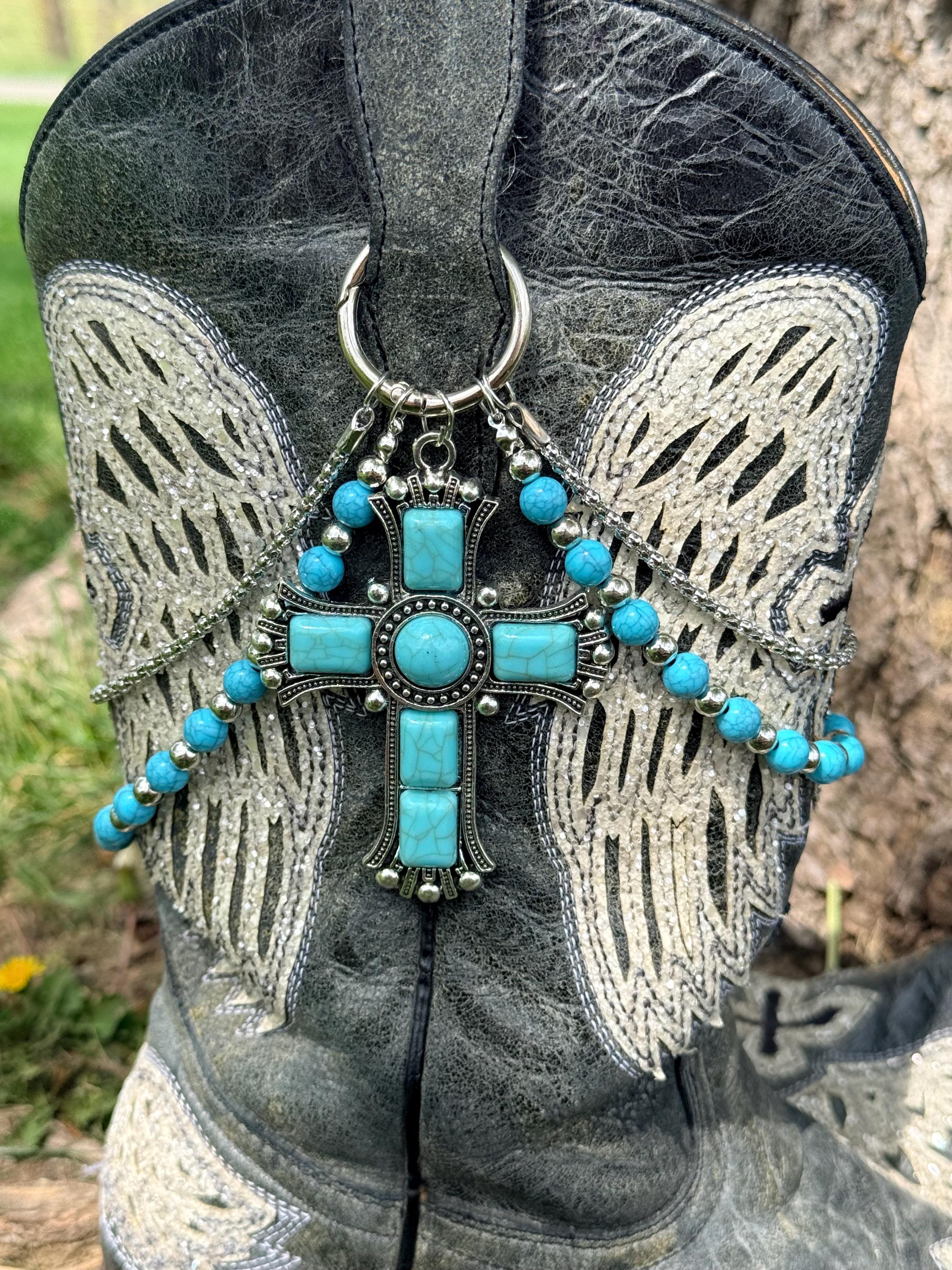 Close-up of black distressed angel wing cowboy boot with two-strand turquoise round bead and silver link chain lei boot bracelet and massive ornate silver cross pendant with multiple turquoise cabochon stones, faith-forward Western boot jewelry