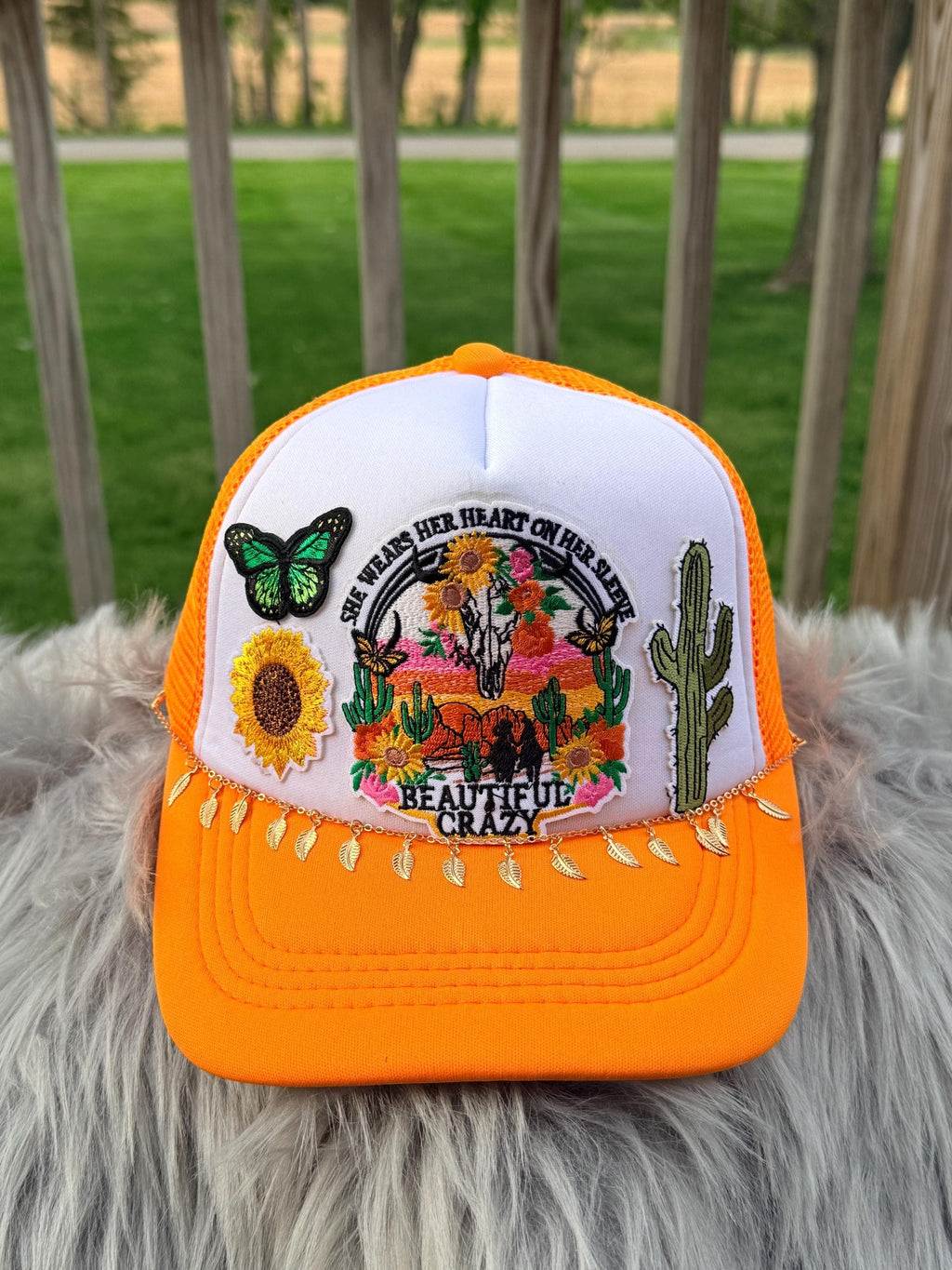 An orange and white trucker hat with a detailed embroidered desert scene on the front panel, 