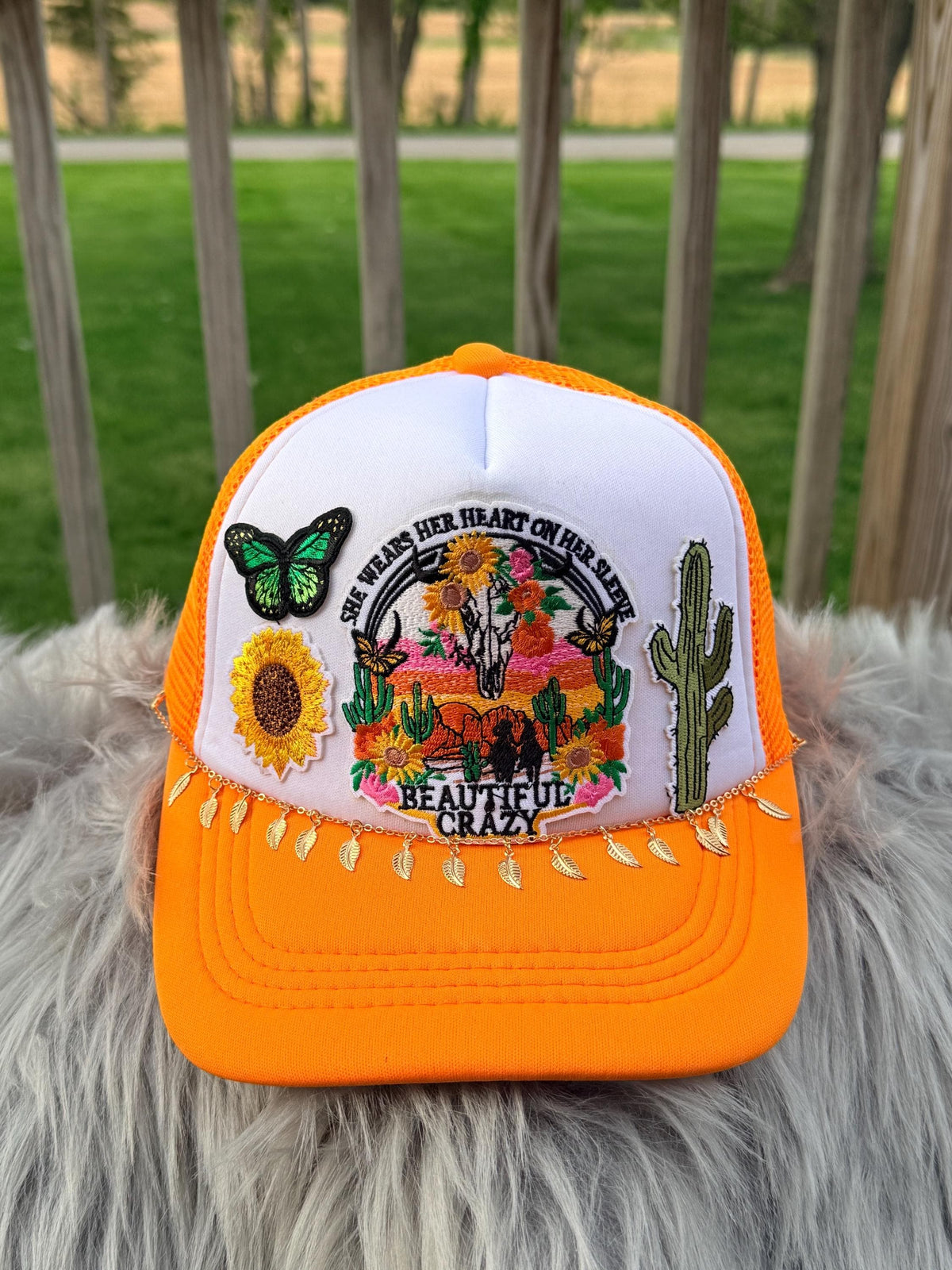 An orange and white trucker hat with a detailed embroidered desert scene on the front panel, 
