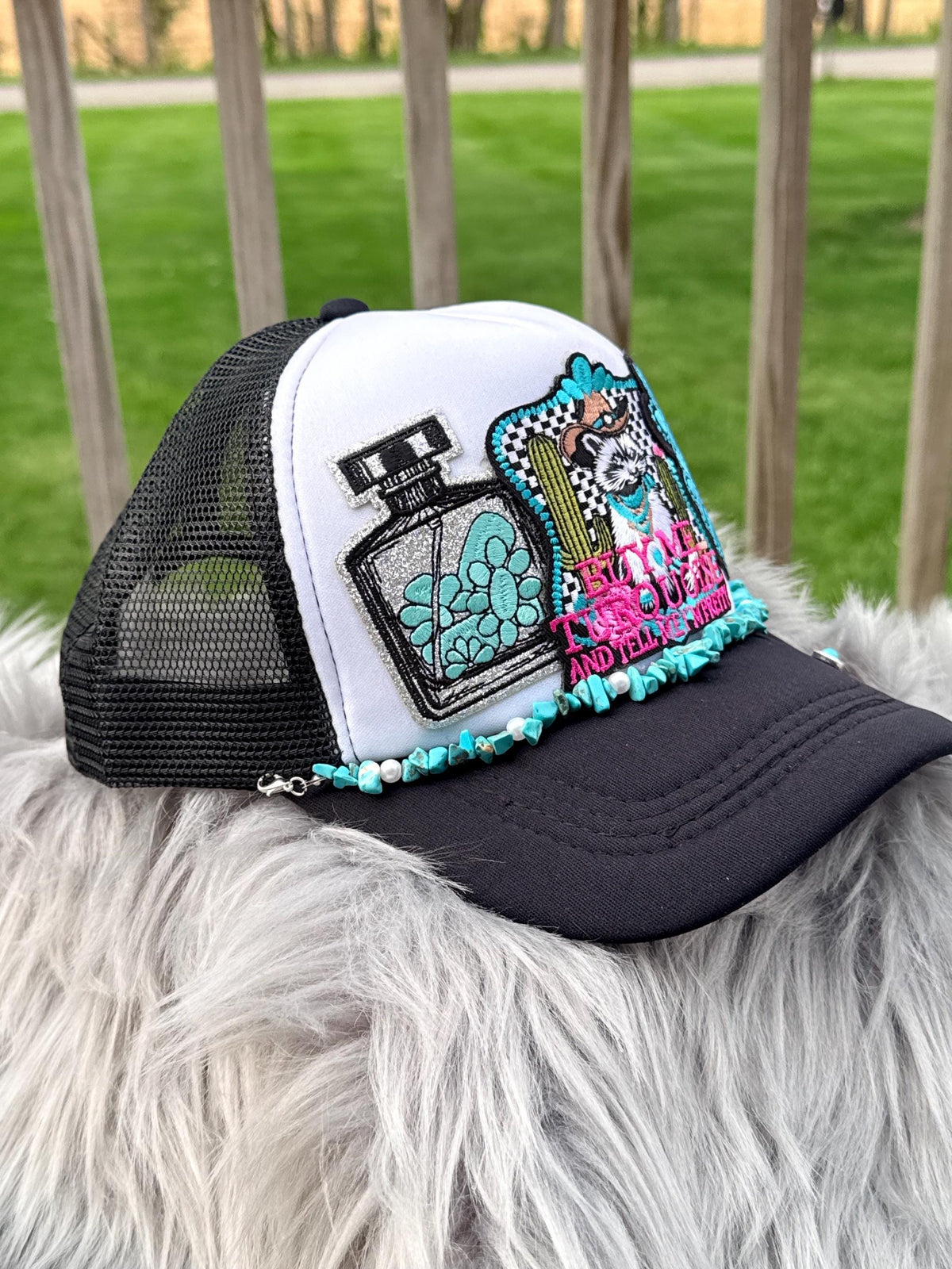A black and white trucker hat with a white front panel, black mesh back, and a large embroidered patch on the side.
