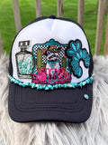 A black and white trucker hat with a detailed embroidered front patch featuring a raccoon, cactus, turquoise flowers, and pink text reading 'BUY ME TURQUOISE AND TELL ME IM PRETTY.' The brim is black with turquoise bead trim, and the back mesh is black.
