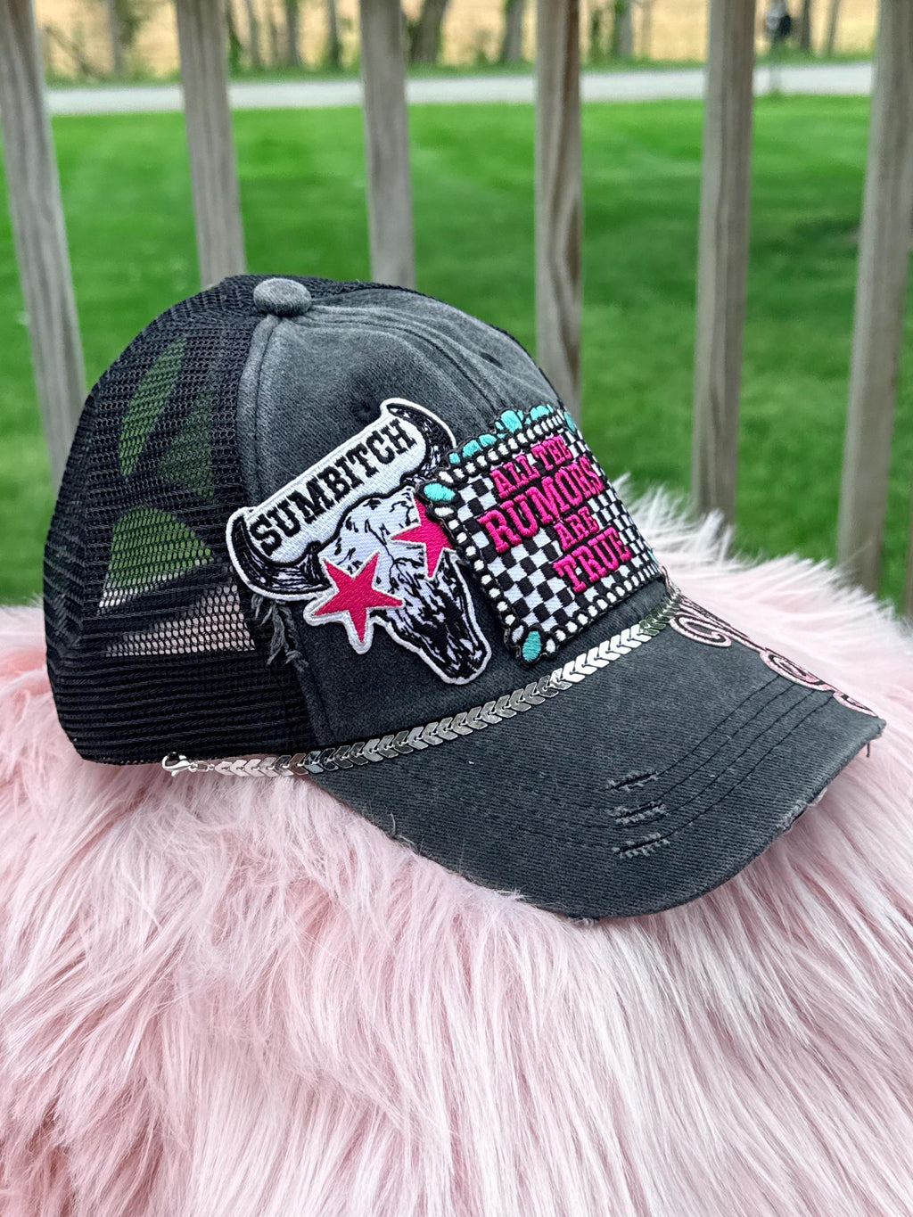 A distressed black trucker hat with mesh back panels, featuring a skull patch with a pink star and the word 'SUMBATCH,'