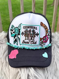 A white and black trucker hat with a black brim, decorated with a 'Cowgirl Social Club' embroidered patch, turquoise beaded trim, a pink rose applique, and a light blue heart applique. 