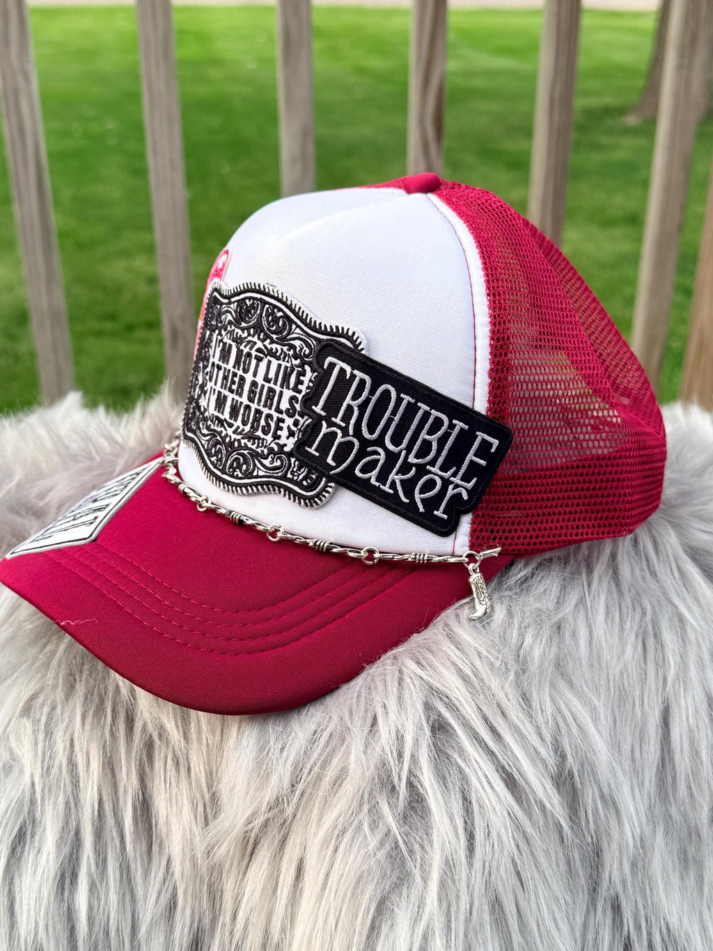 A red and white trucker hat with a black embroidered patch reading 'Trouble Maker'