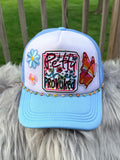 A light blue and white trucker hat with colorful embroidered details, including flowers, a butterfly, and the text 'Pretty When Provoked,'