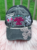 A distressed charcoal gray trucker hat with multiple embroidered patches and rhinestone trim,