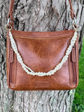 Front view of brown leather Bandana crossbody bag against tree with 16-inch Western boho twisted faux pearl strand purse chain featuring two twisted strands of mixed-size round and seed pearls in rope-style construction clipped via gold rings to bag hardware