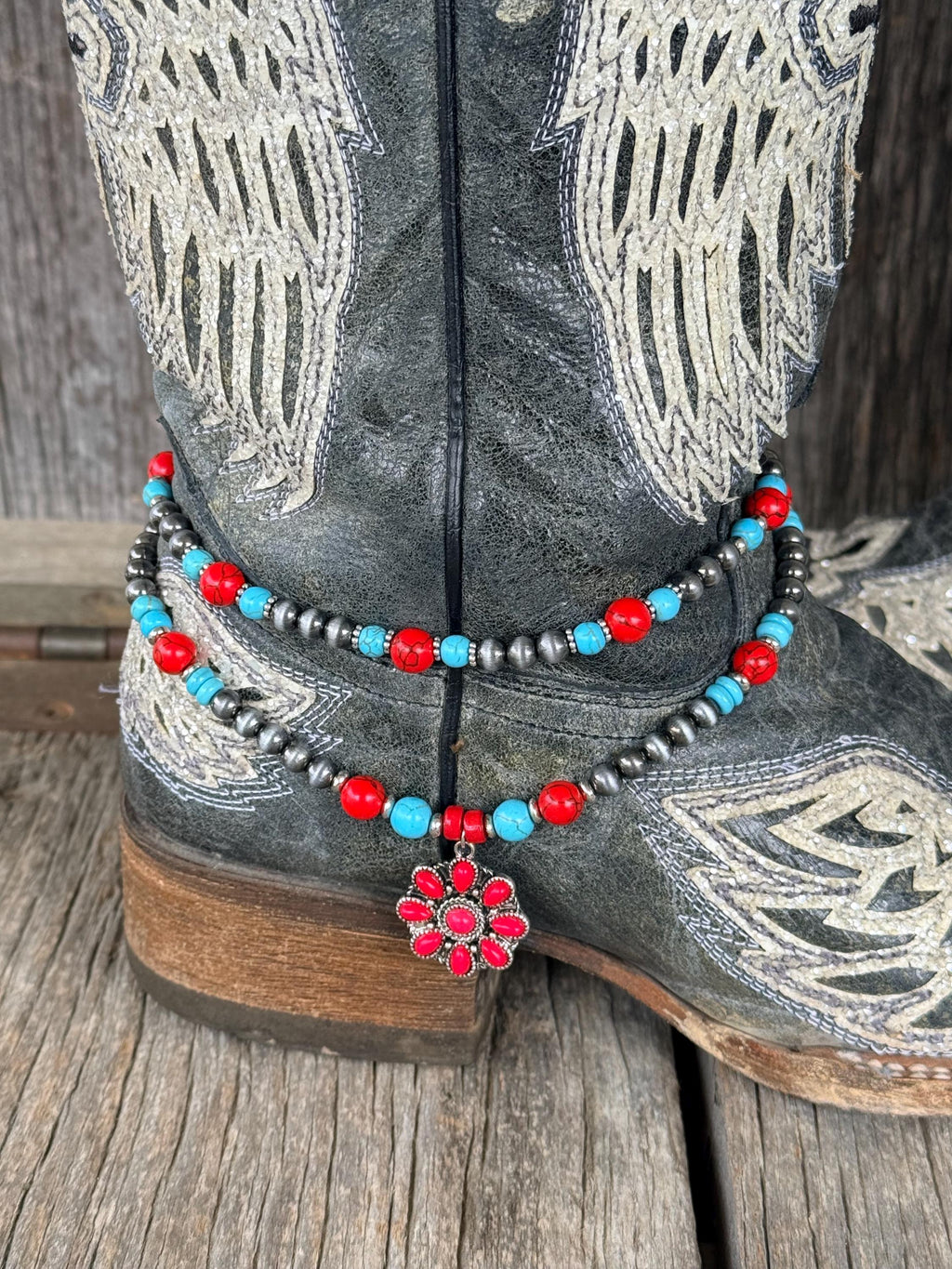 Close-up of beaded boot bracelet on black cowboy boot featuring turquoise, red, and silver Navajo pearl beads with a red flower charm pendant