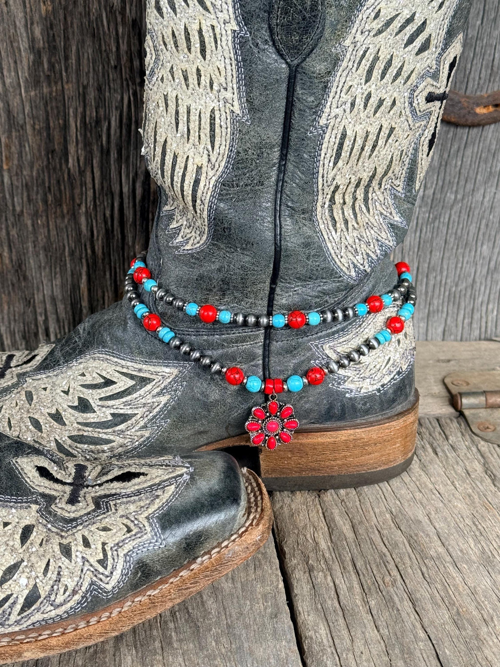 Side view of Western beaded boot bracelet with turquoise, red, and silver beads and red flower charm on black embroidered cowboy boot