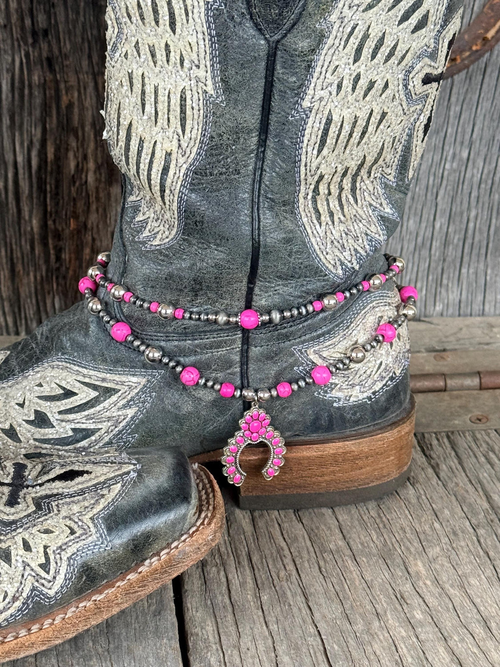 Side angle of black angel wing cowboy boots with double-strand pink and silver beaded boot bracelet and pink squash blossom charm