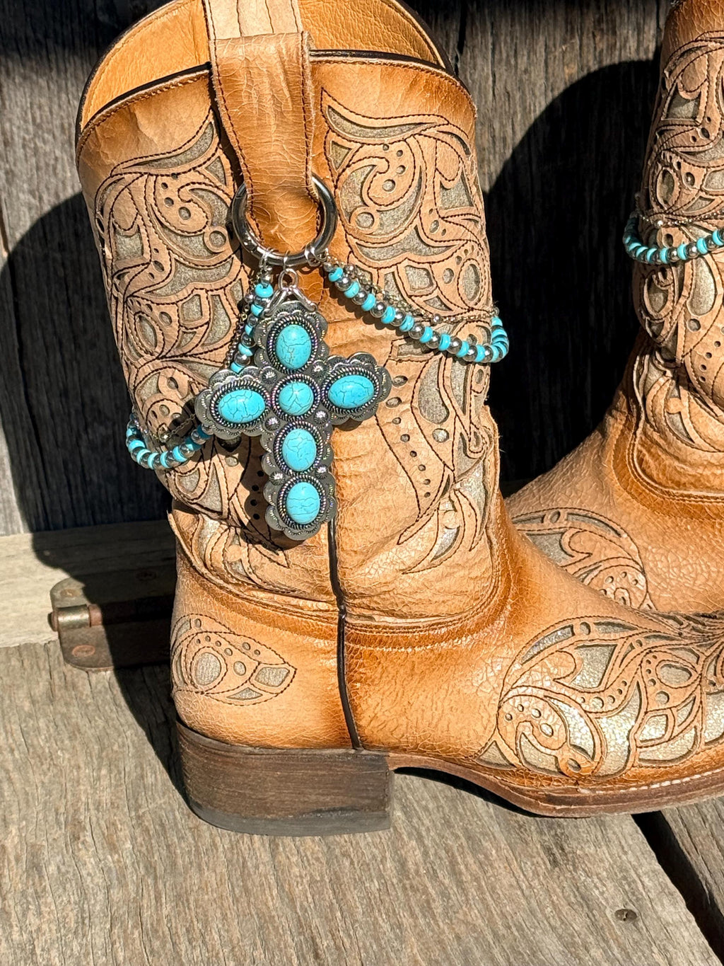 Close-up of tan tooled leather cowboy boot wearing turquoise beaded boot bracelet with large silver turquoise cross concho charm pendant, Western boot jewelry