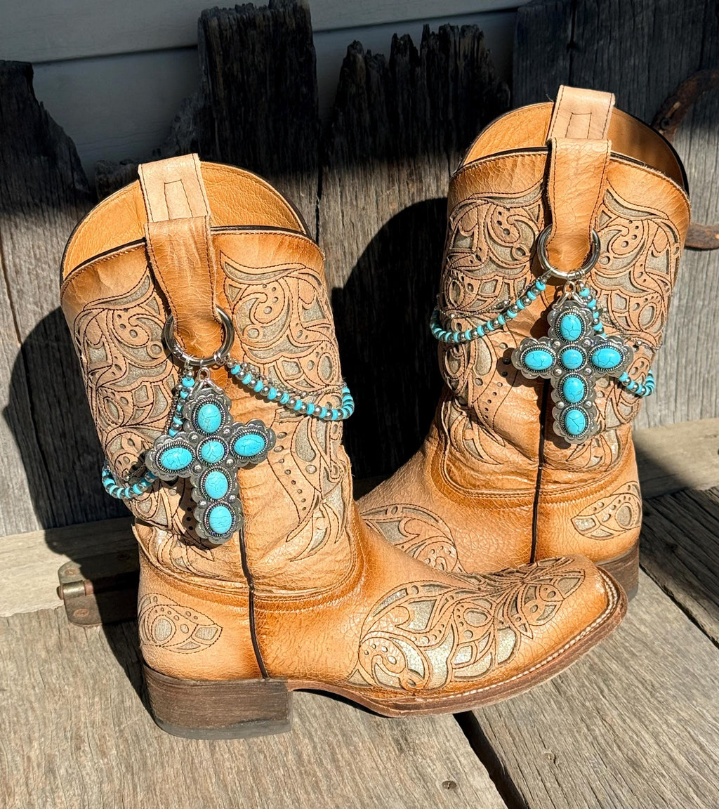 Pair of tan tooled leather cowboy boots on rustic wood planks wearing turquoise beaded boot bracelets with large silver turquoise cross concho charms, set of 2