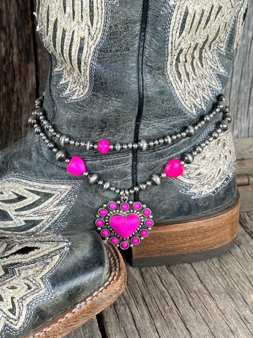 Close-up of double-strand silver and hot pink beaded boot bracelet on black angel wing cowboy boot with large ornate pink rhinestone heart concho charm