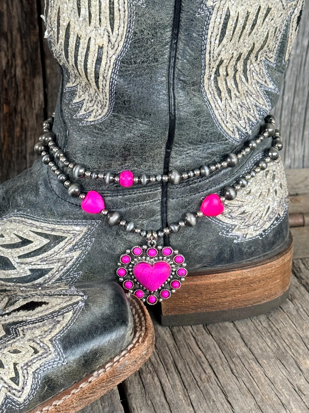 Close-up of double-strand silver and hot pink beaded boot bracelet on black angel wing cowboy boot with large ornate pink rhinestone heart concho charm
