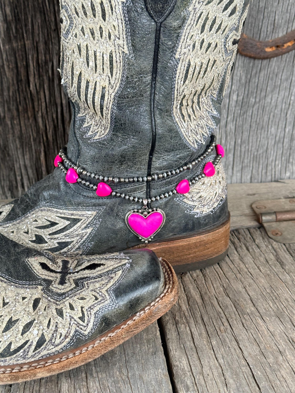 Side angle of black angel wing cowboy boots with double-strand silver and hot pink beaded boot bracelet and pink enamel heart charm