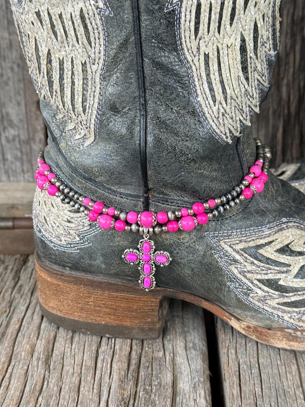 Close-up of double-strand pink and silver beaded boot bracelet on black angel wing cowboy boot with pink rhinestone cross charm pendant