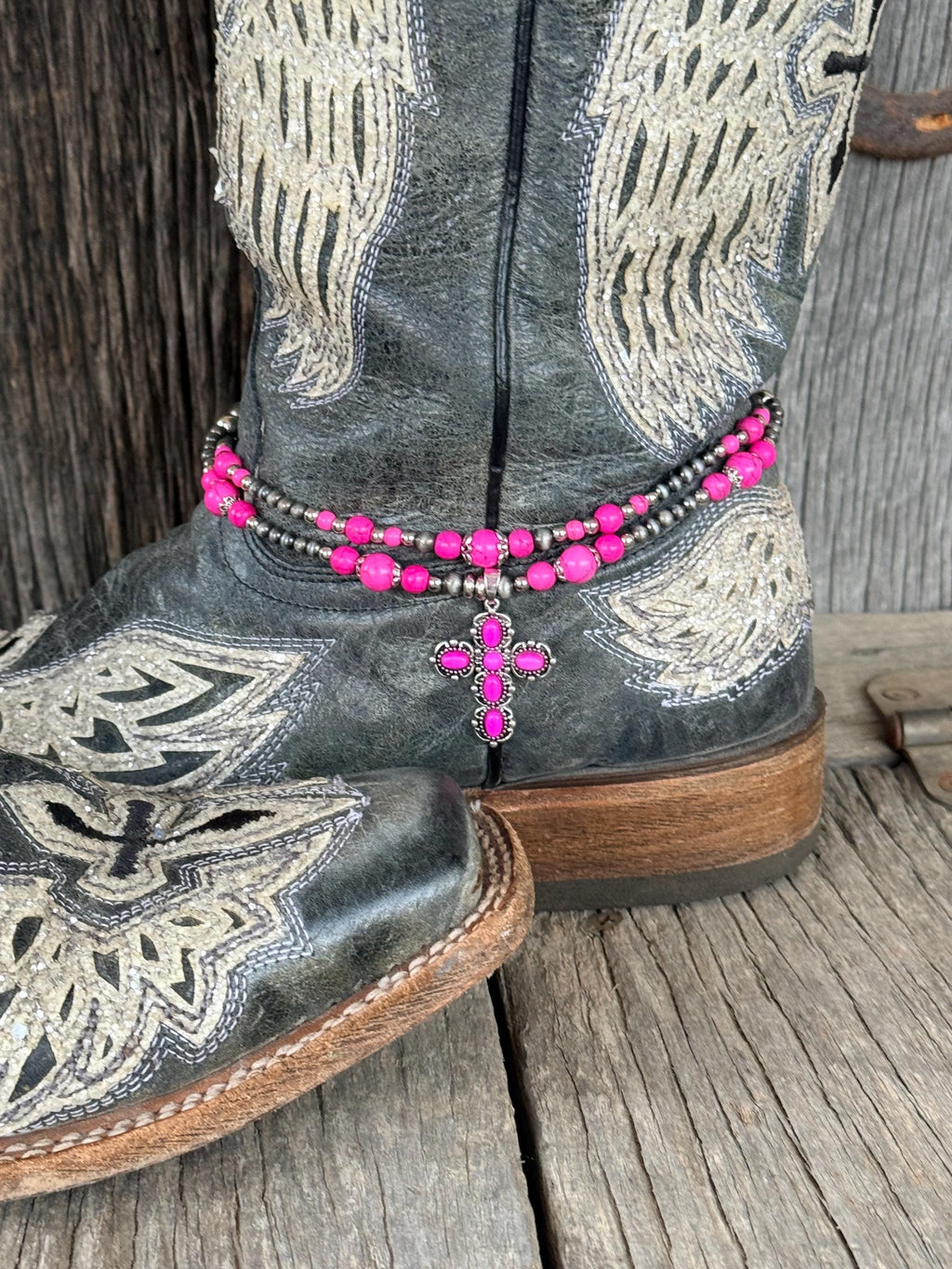 Side angle of black angel wing cowboy boot with double-strand pink and silver beaded boot bracelet and pink rhinestone cross charm