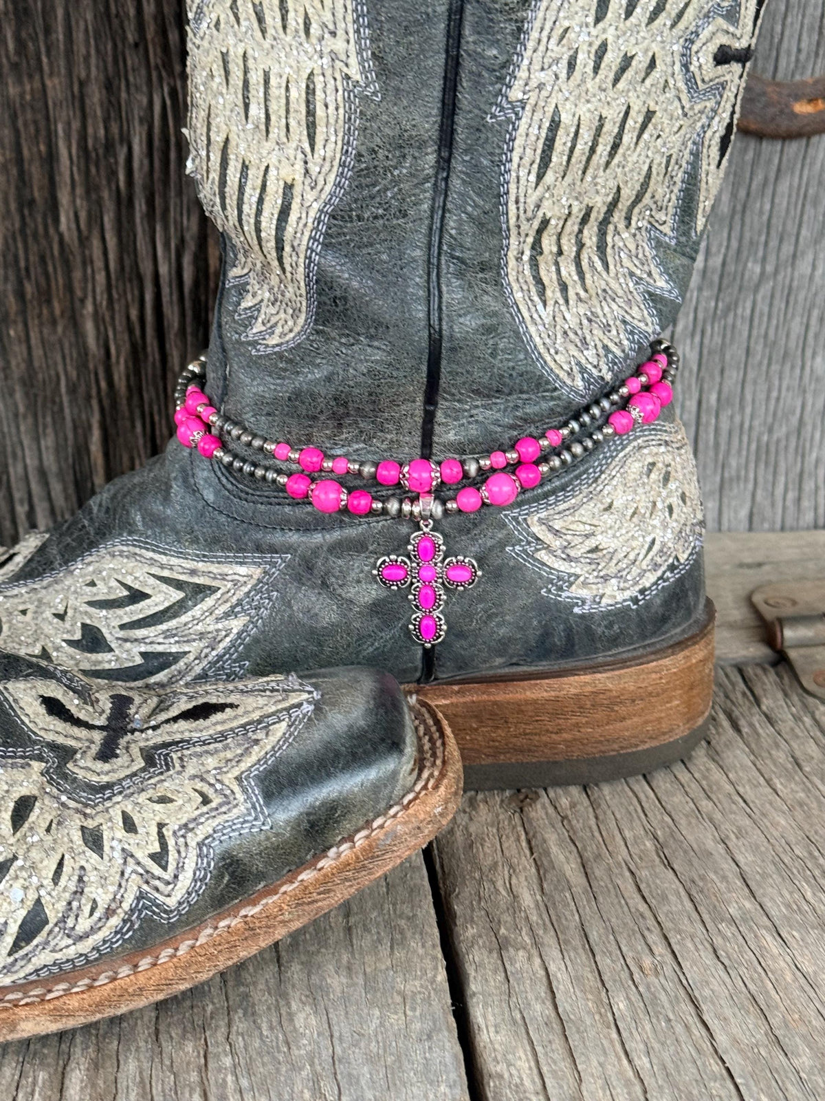 Side angle of black angel wing cowboy boot with double-strand pink and silver beaded boot bracelet and pink rhinestone cross charm