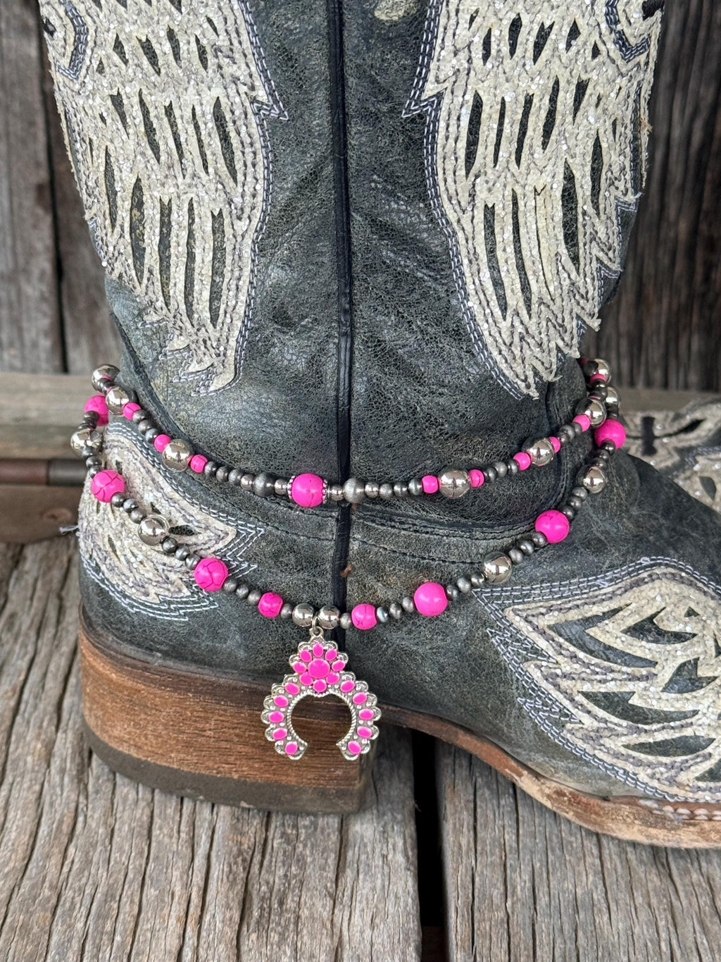 Close-up of double-strand pink and silver beaded boot bracelet on black angel wing cowboy boot with pink squash blossom charm pendant