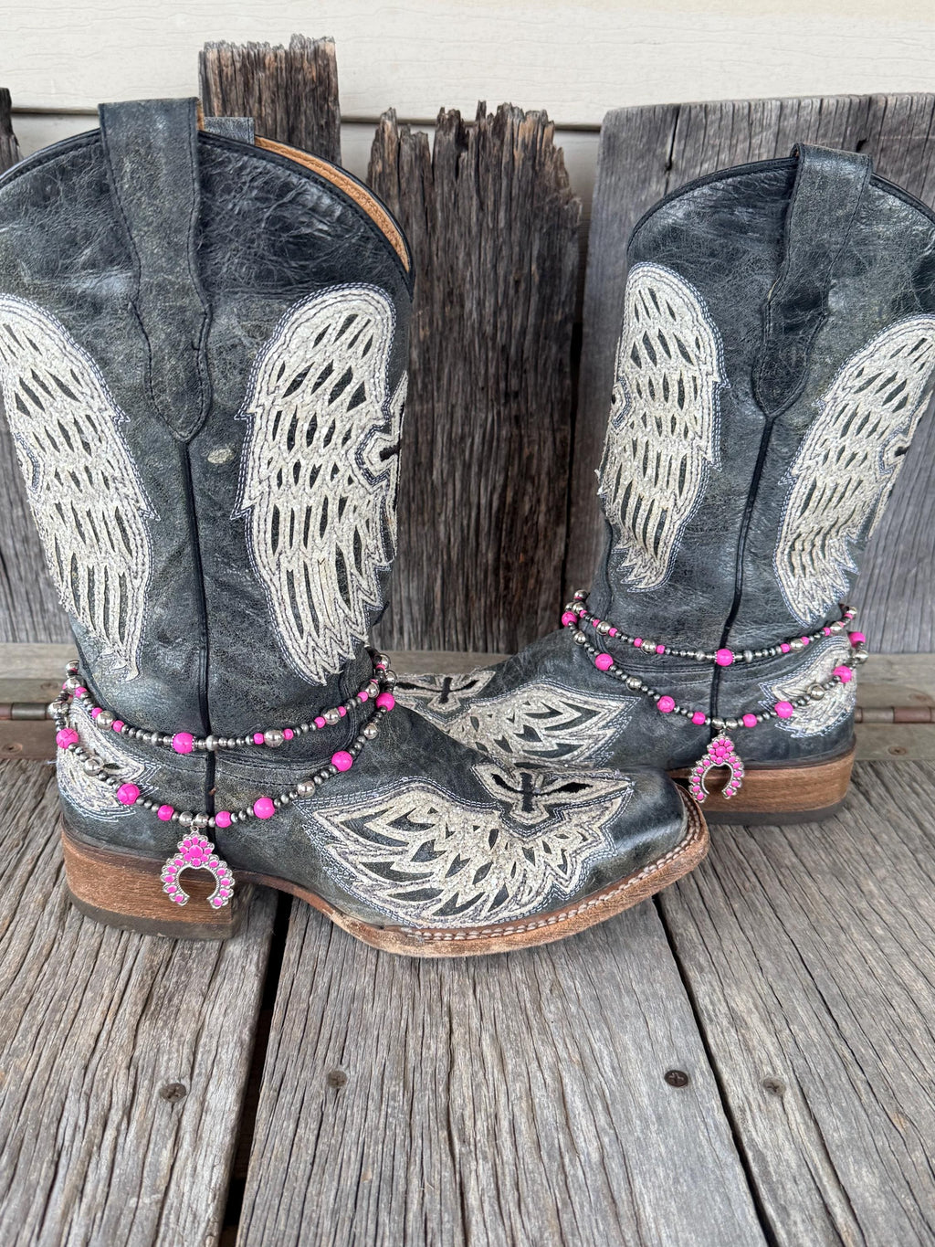 Pair of black angel wing embroidered cowboy boots wearing double-strand pink and silver beaded boot bracelets with pink squash blossom charms, set of 2
