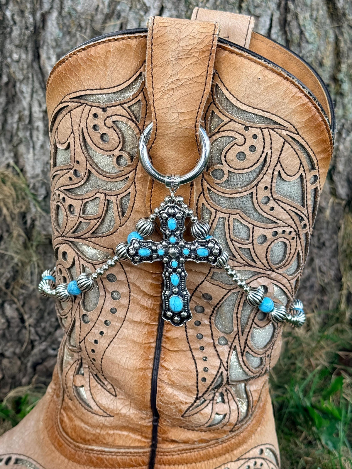 Front view of tan laser-cut scrollwork cowboy boot with silver ball chain and turquoise round bead boot bracelet lei with silver ribbed spacers and large ornate silver cross pendant with turquoise cabochon stones