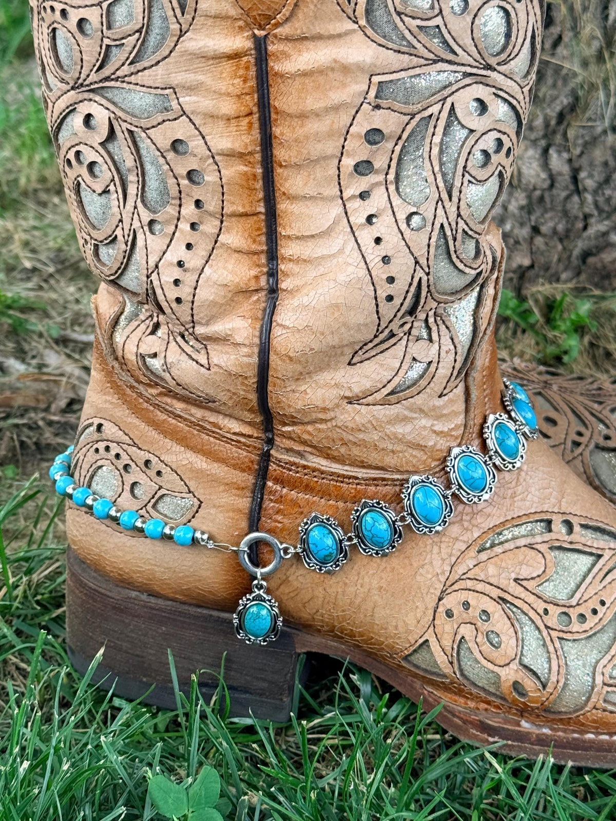 Back heel view of tan tooled laser-cut cowboy boot with two-strand silver and turquoise boot bracelet featuring oval concho strand, bead strand, and turquoise drop charm, Western boho boot jewelry
