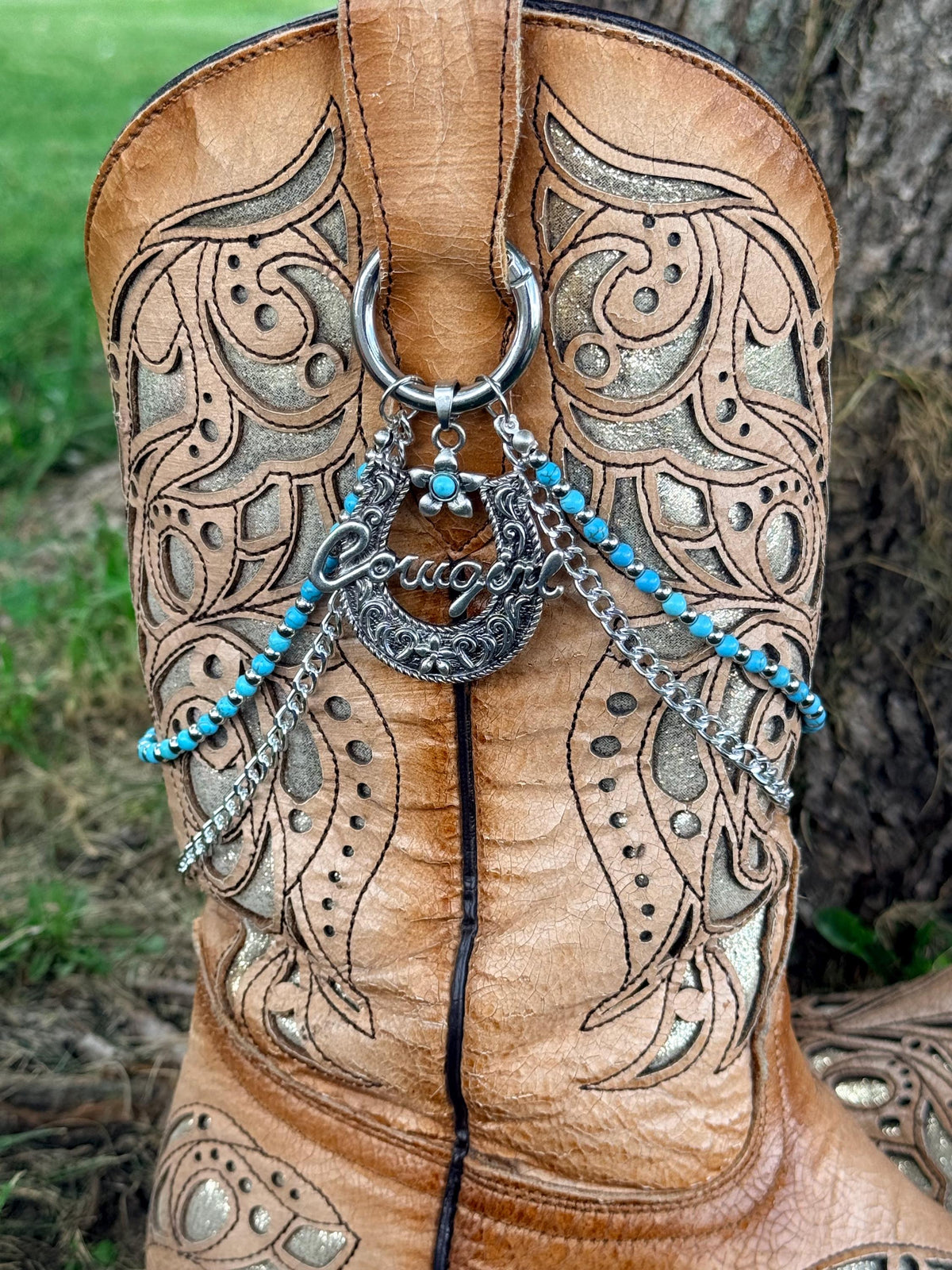Close-up of tan tooled laser-cut cowboy boot shaft with two-strand lei boot bracelet featuring large silver horseshoe charm with turquoise flower accent, turquoise bead strand and silver link chain strand