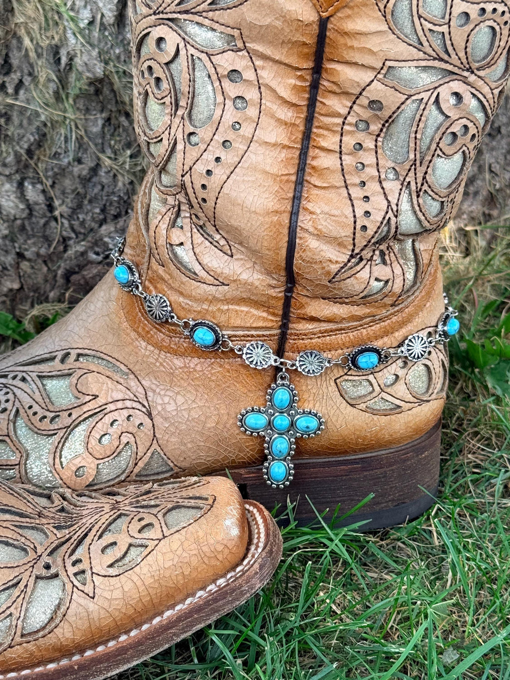 Front view of tan tooled laser-cut cowboy boot with silver and turquoise concho chain boot bracelet and large six-stone turquoise cross pendant drop, Western boho boot accessory