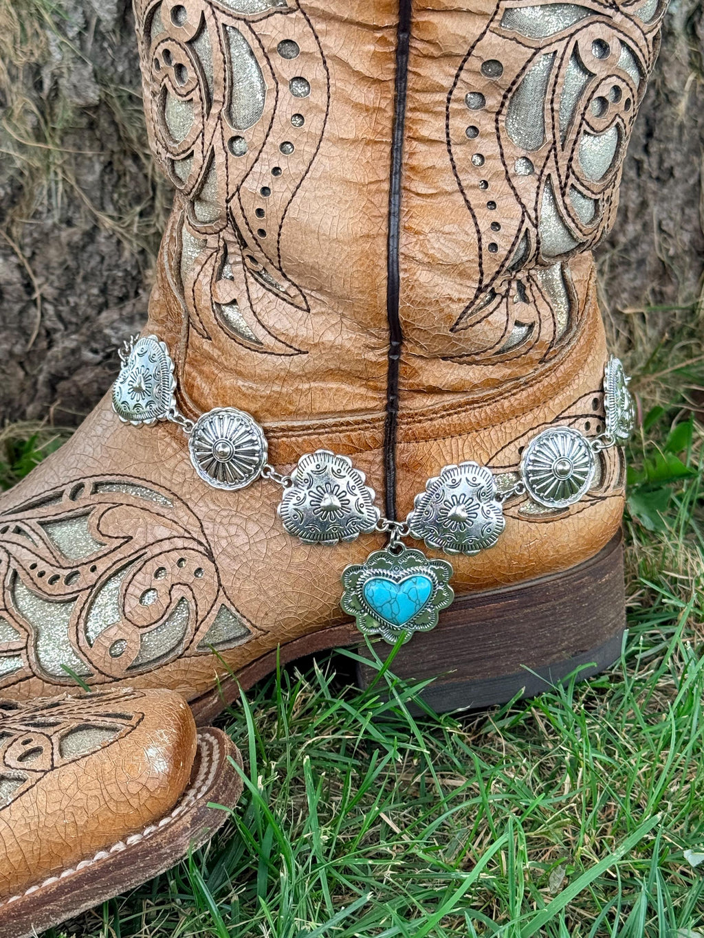 Close-up of tan tooled laser-cut cowboy boot ankle with silver concho chain boot bracelet featuring five linked silver conchos and a large turquoise heart drop charm pendant