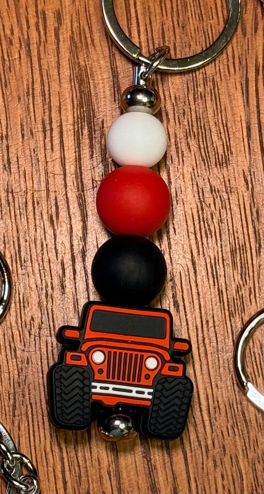 A close-up of a beaded keychain featuring a red and black off-road vehicle charm, with white and black beads, resting on a wooden surface.