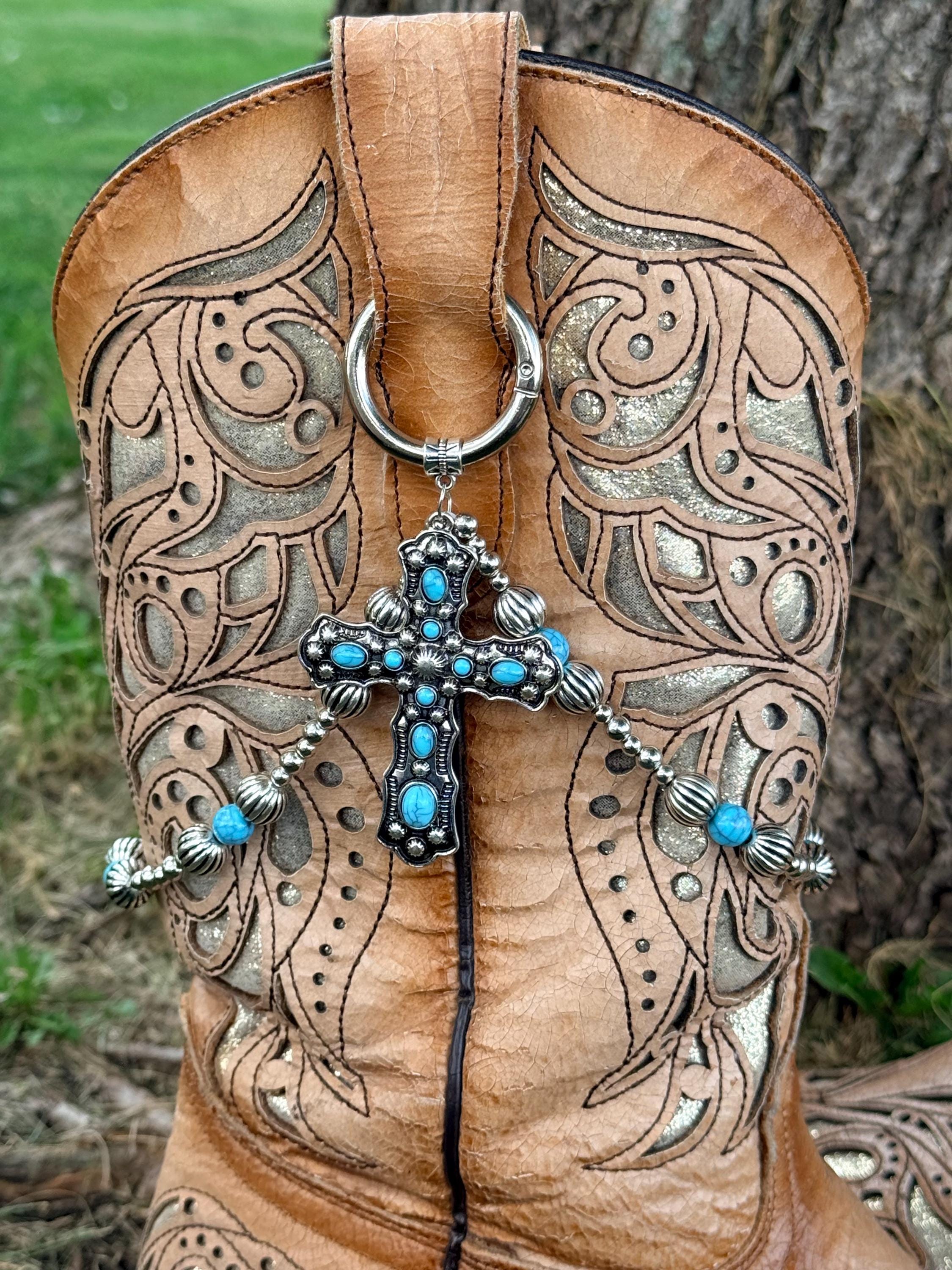 Close-up of tan laser-cut scrollwork cowboy boot shaft with silver ball chain and turquoise bead boot bracelet lei featuring large ornate silver cross pendant set with multiple turquoise cabochon stones, clipped through boot pull loop ring