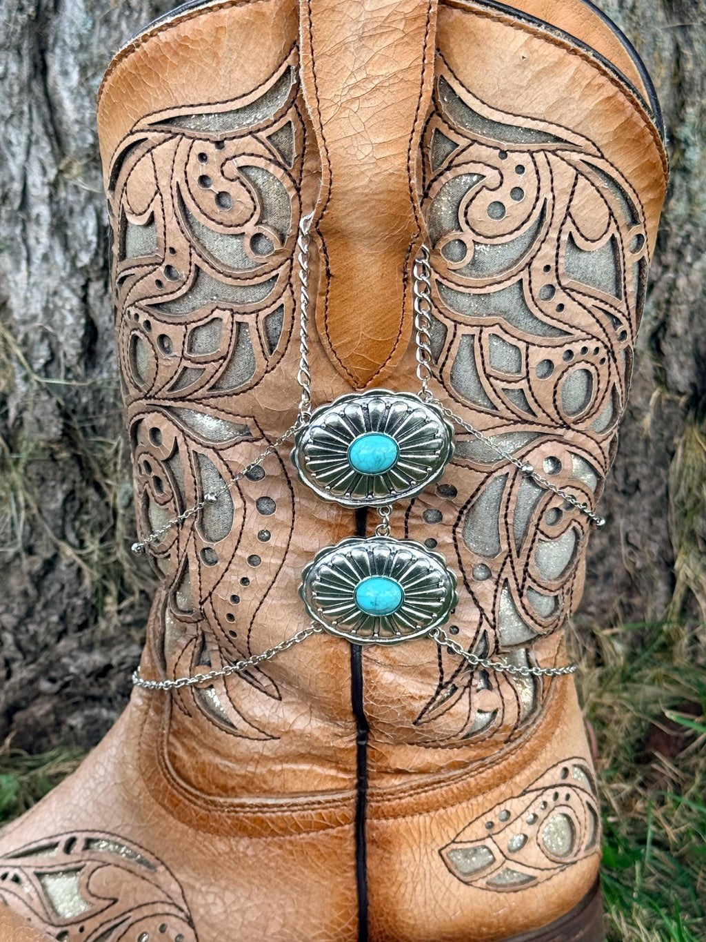 Front close-up of tan tooled laser-cut cowboy boot with layered silver chain boot bracelet and two stacked turquoise stone oval concho charms, Western boho boot accessory